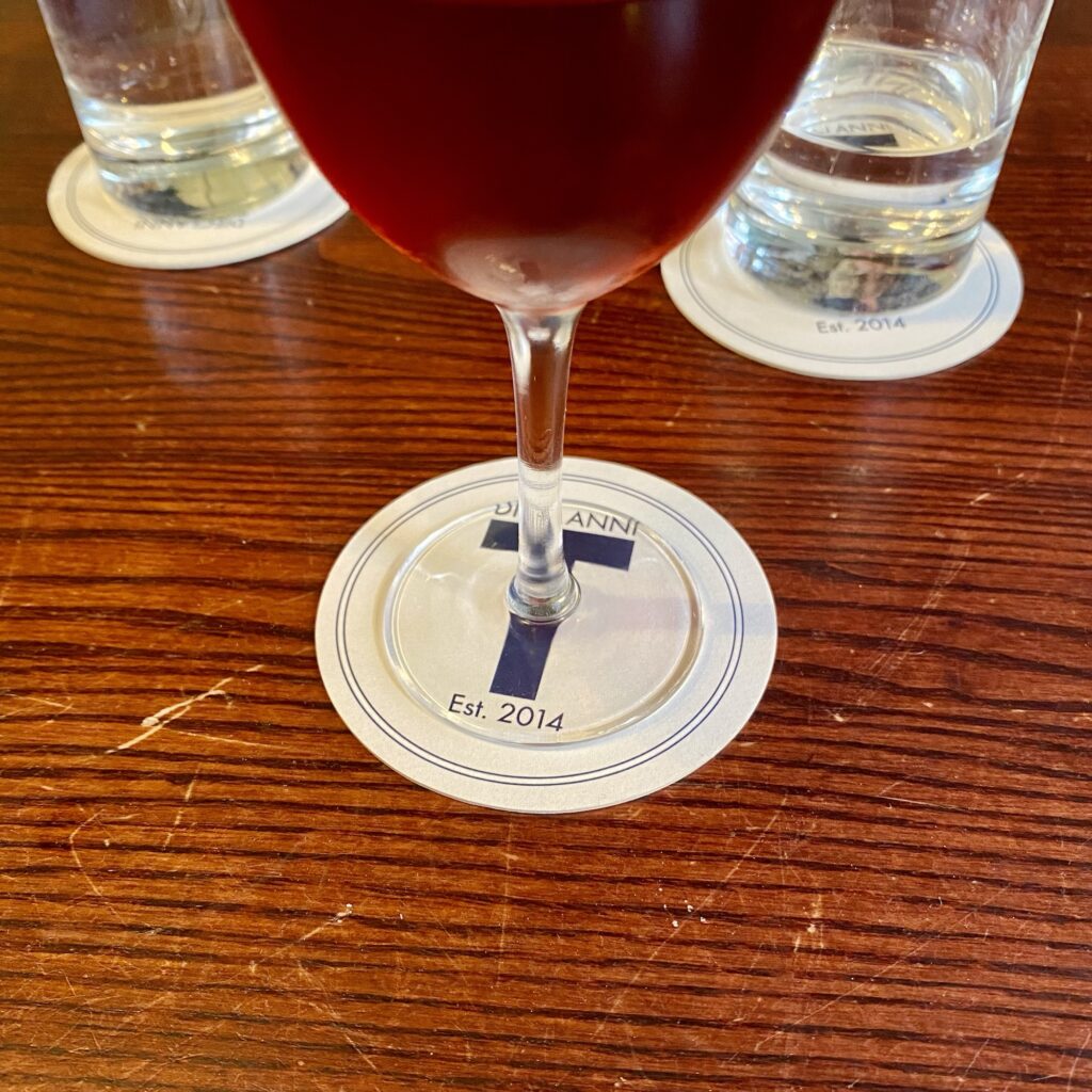 A glass of red beverage resting on a circular coaster with the letter 'T' and 'Est. 2014' printed on it.