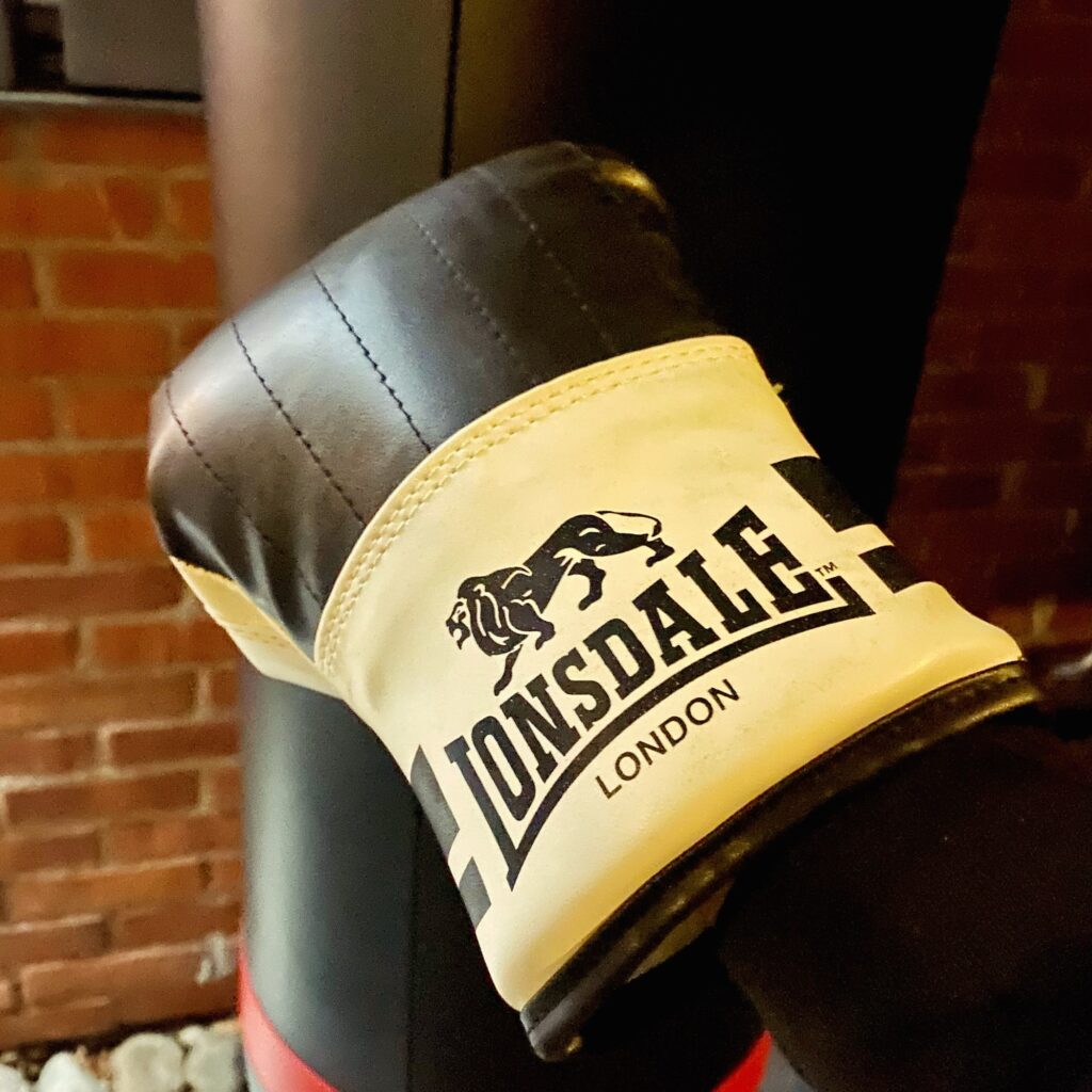 Black and white boxing glove with Lonsdale branding positioned against a punching bag.