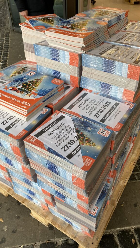 Stack of printed toy catalogues with colourful covers and visible barcodes, arranged on a wooden pallet.