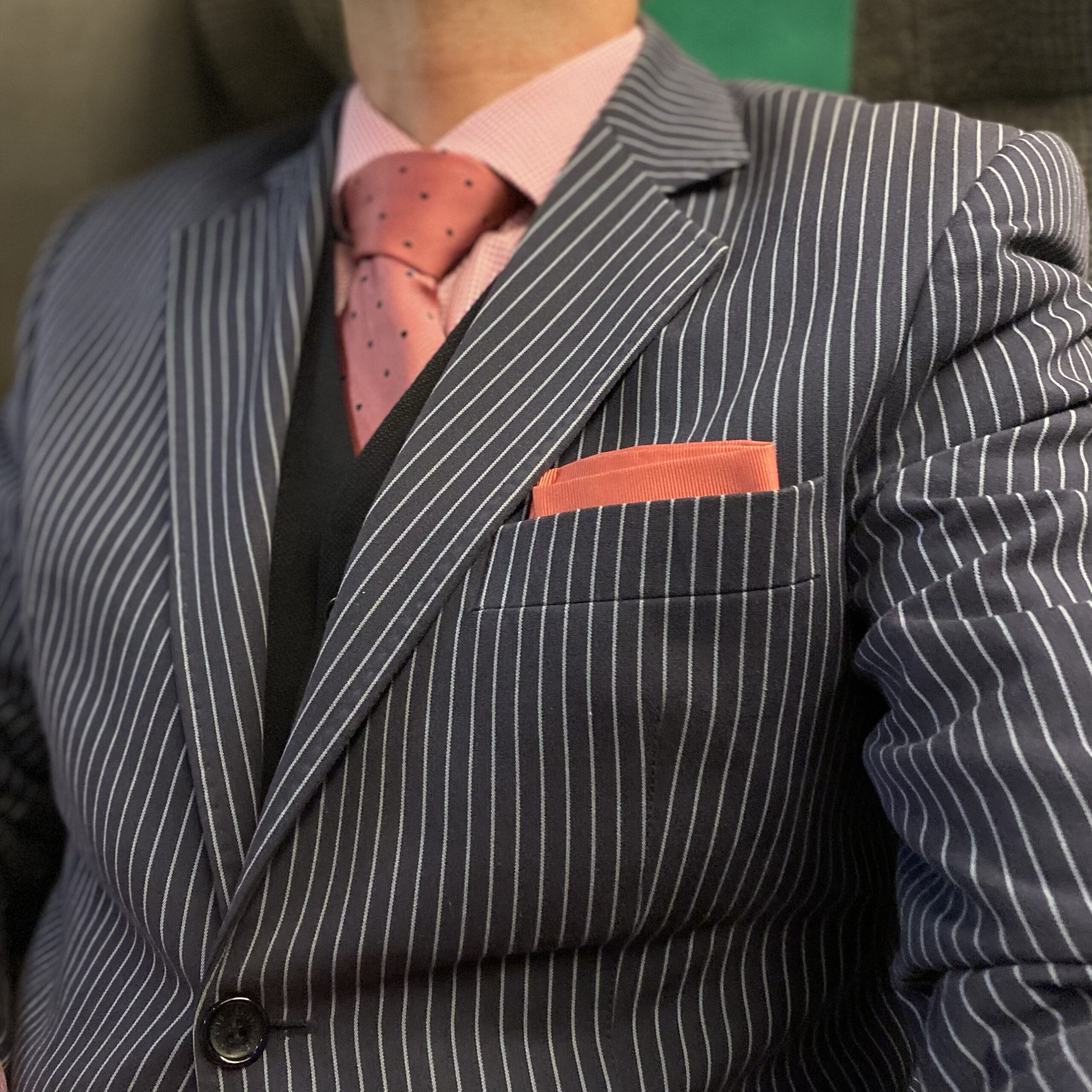 Striped suit with a pink shirt and tie, complemented by a pocket square in a contrasting colour.