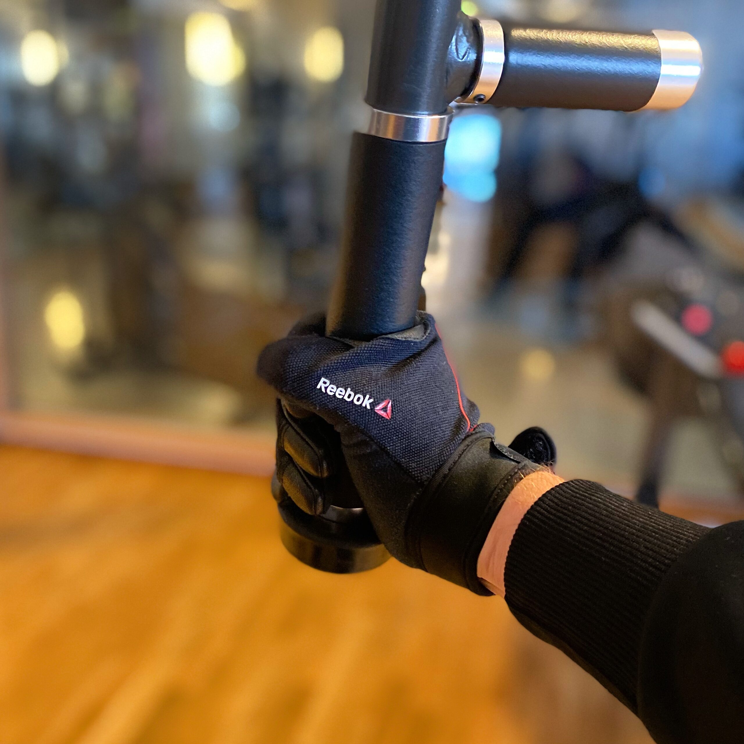 A hand wearing a Reebok fitness glove gripping the handle of gym equipment in a fitness setting.