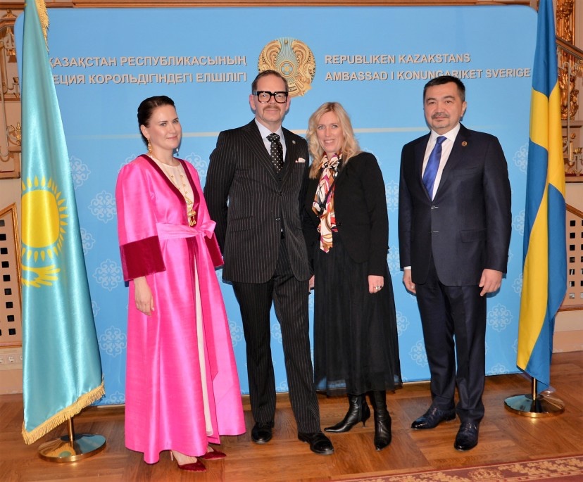 Four individuals posing together in formal attire against a backdrop featuring the flags of Kazakhstan and Sweden.