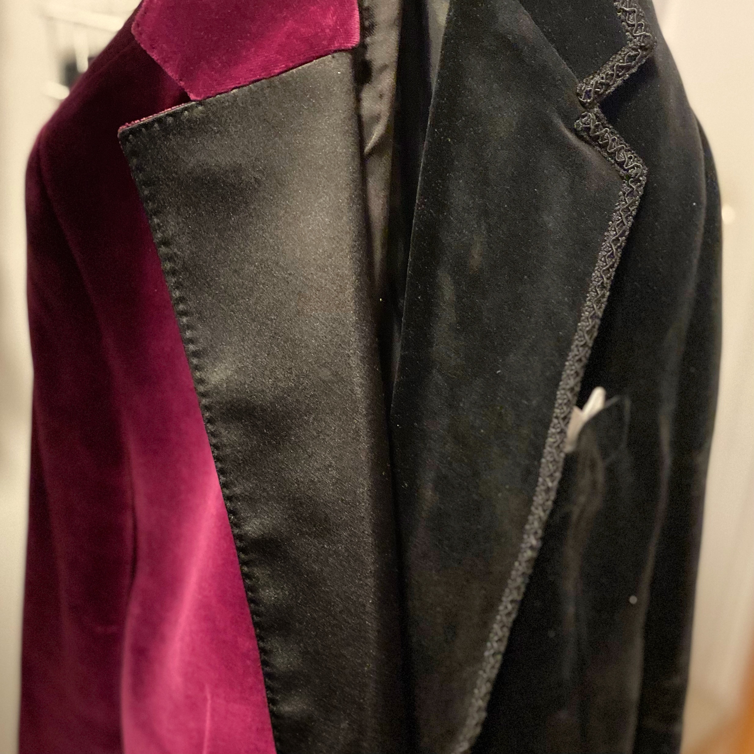 A close-up view of a red velvet jacket and a black velvet jacket displayed together on a hanger.