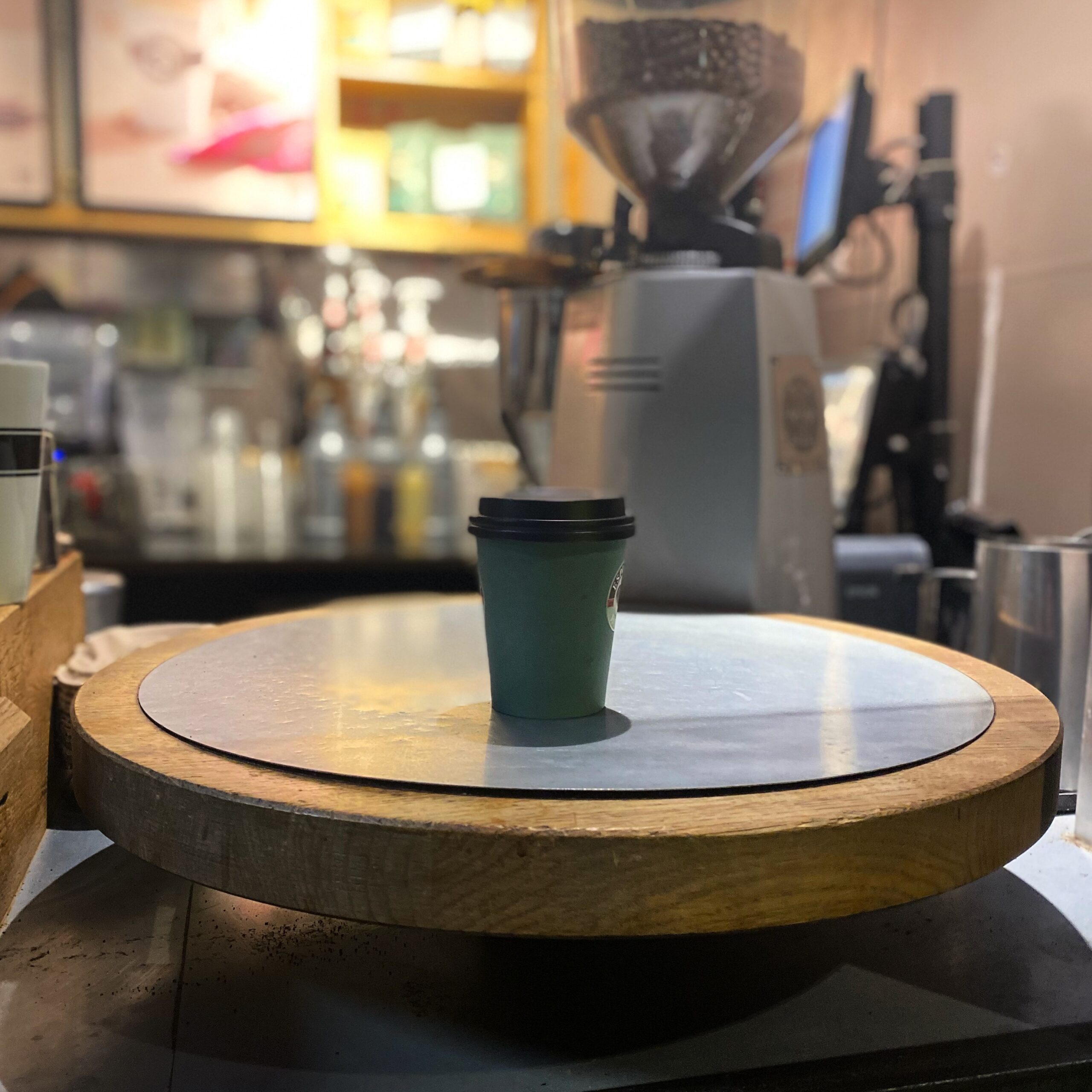 A green takeaway coffee cup placed on a wooden rotating display in a café environment.