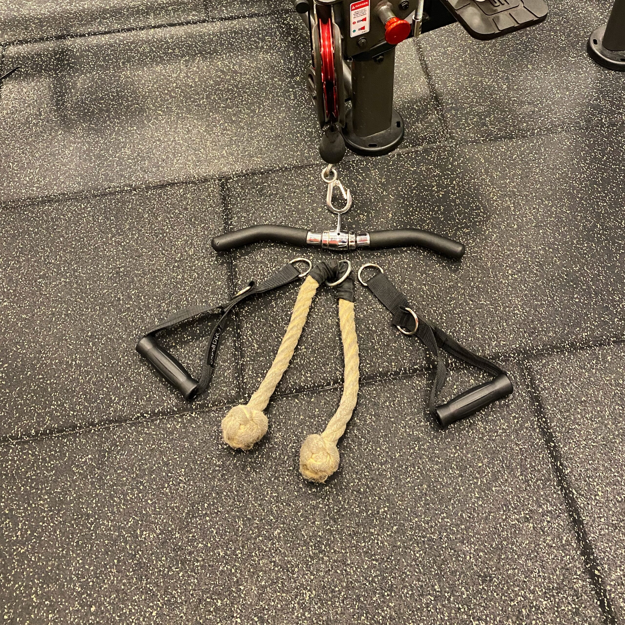 Gym equipment attachment with a straight bar and two rope handles on a rubber floor.