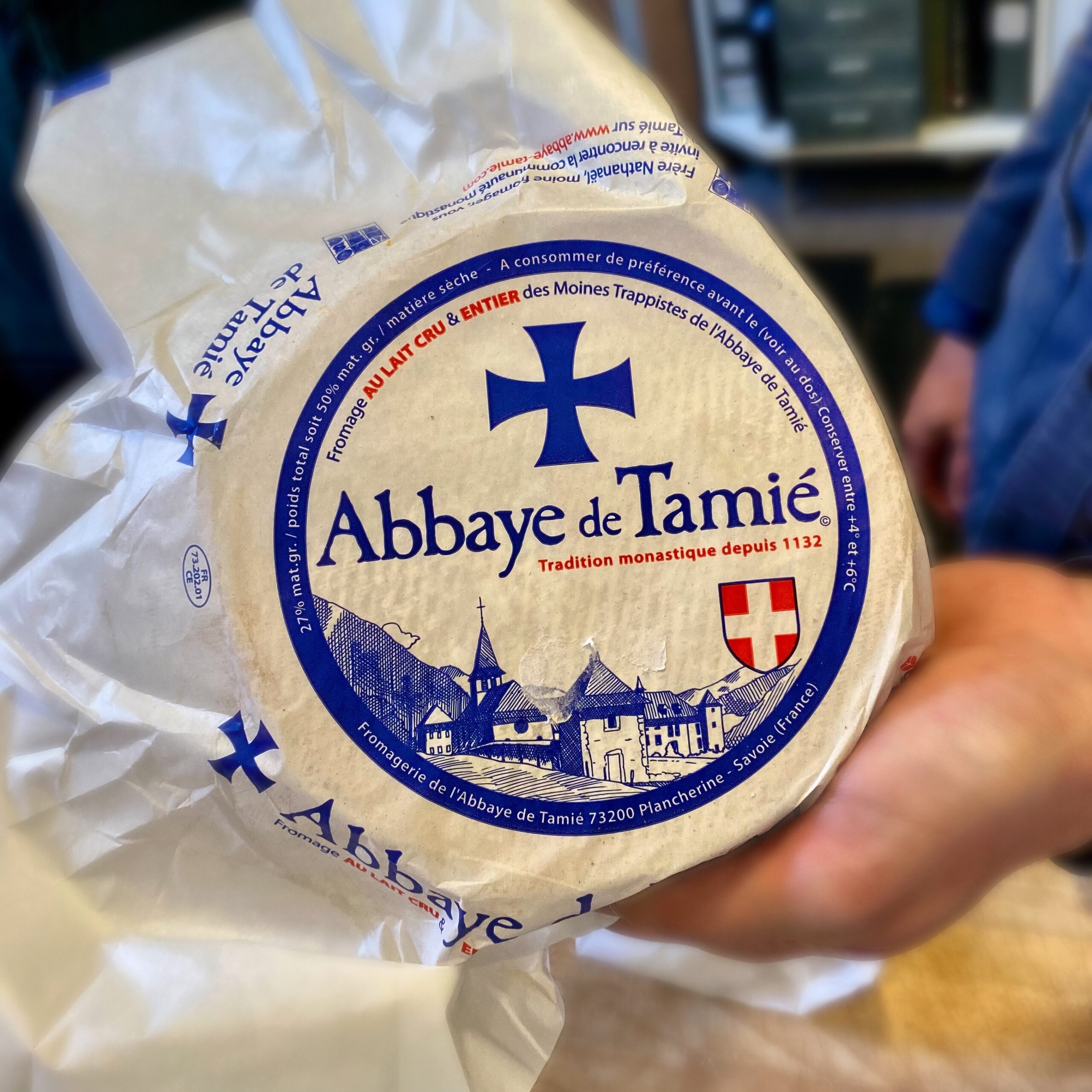 Round cheese wheel labelled 'Abbaye de Tamie' with a blue cross and monastery illustration.