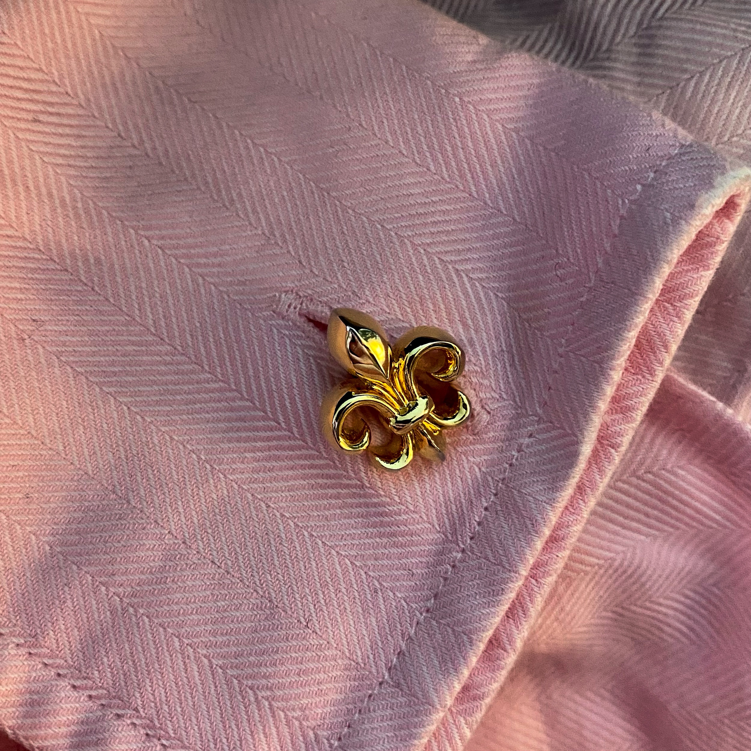Gold fleur-de-lis pin attached to a pink textured fabric shirt.