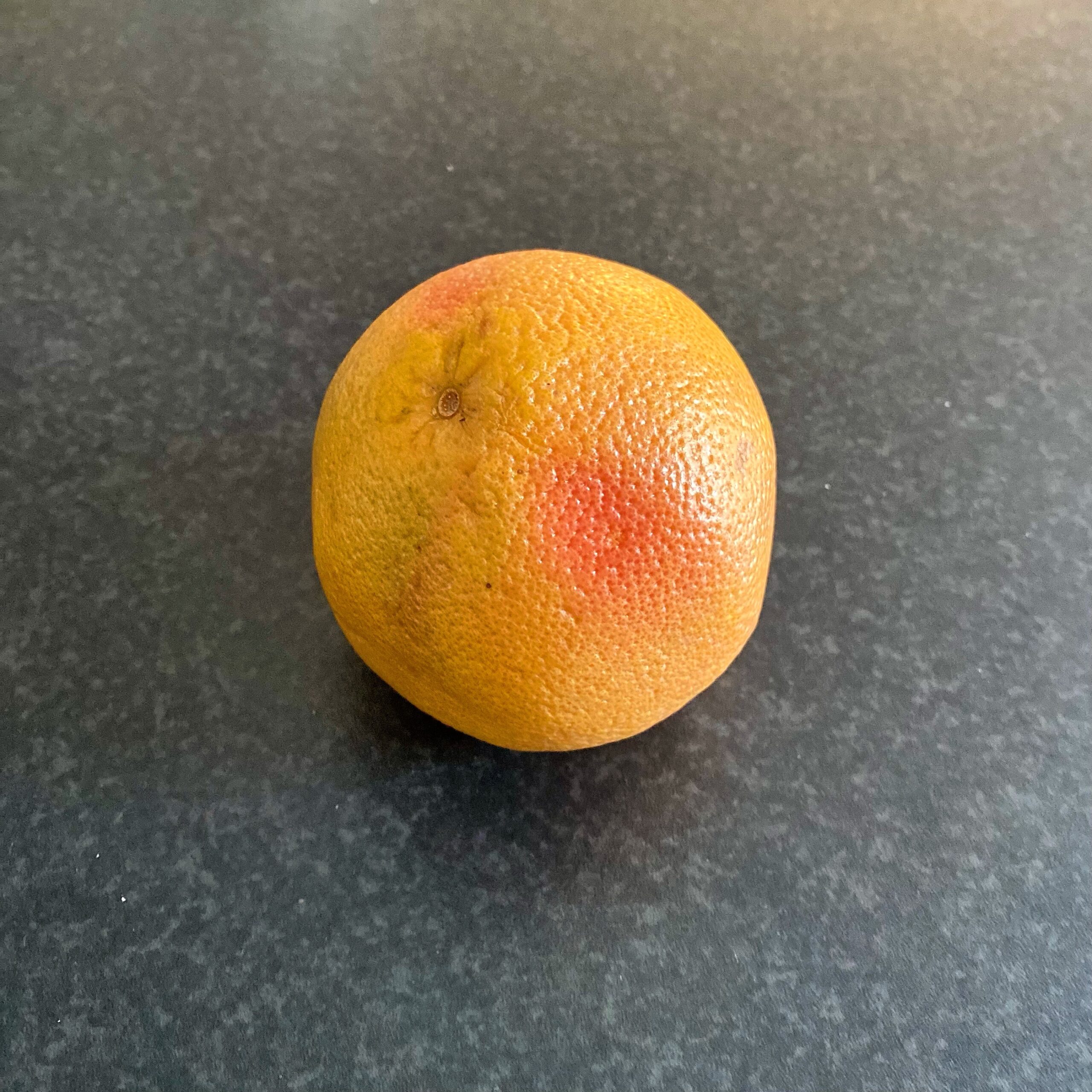 A single grapefruit with a slightly textured skin, displaying shades of yellow and pink.