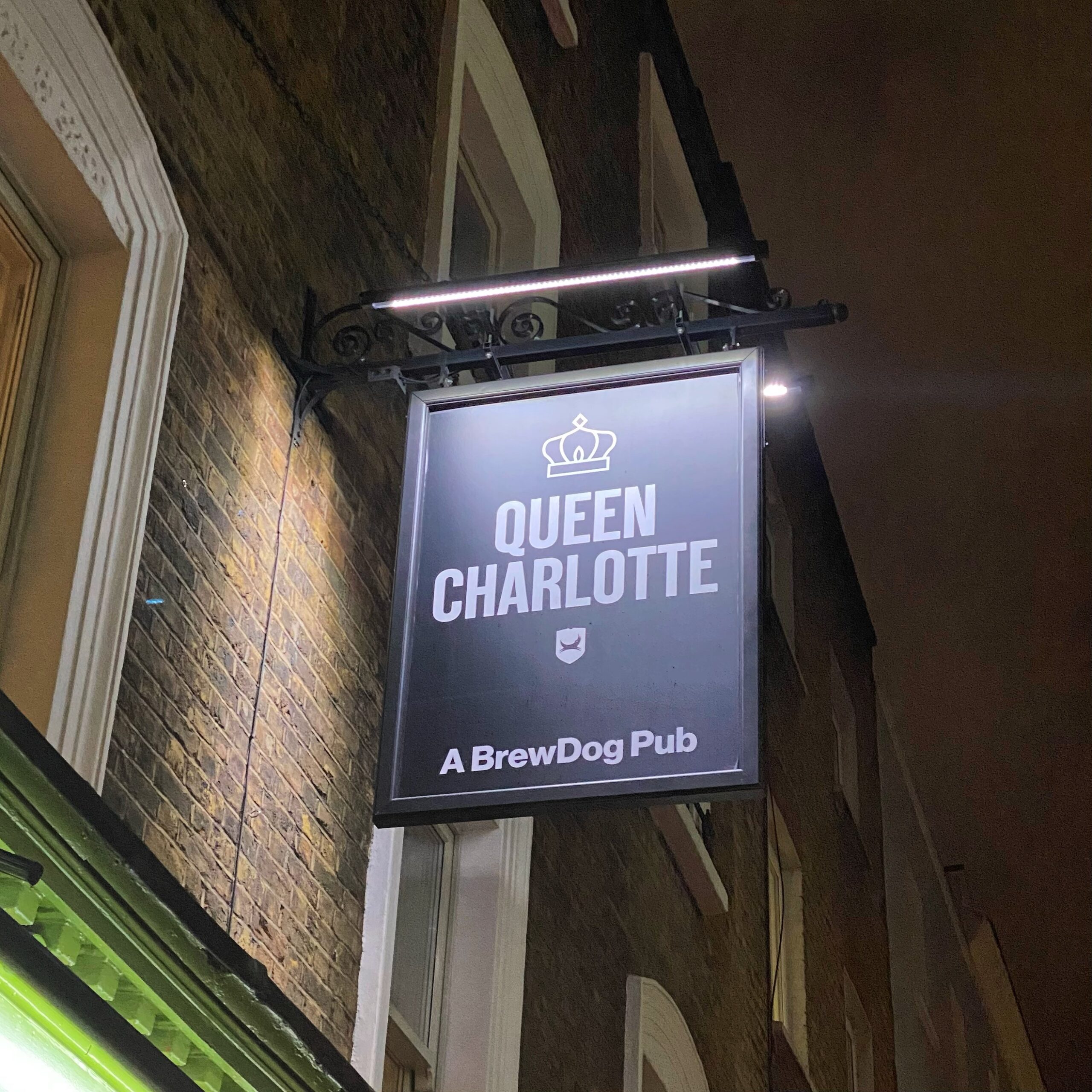 Sign for Queen Charlotte, a BrewDog pub, displayed on a building exterior at night.