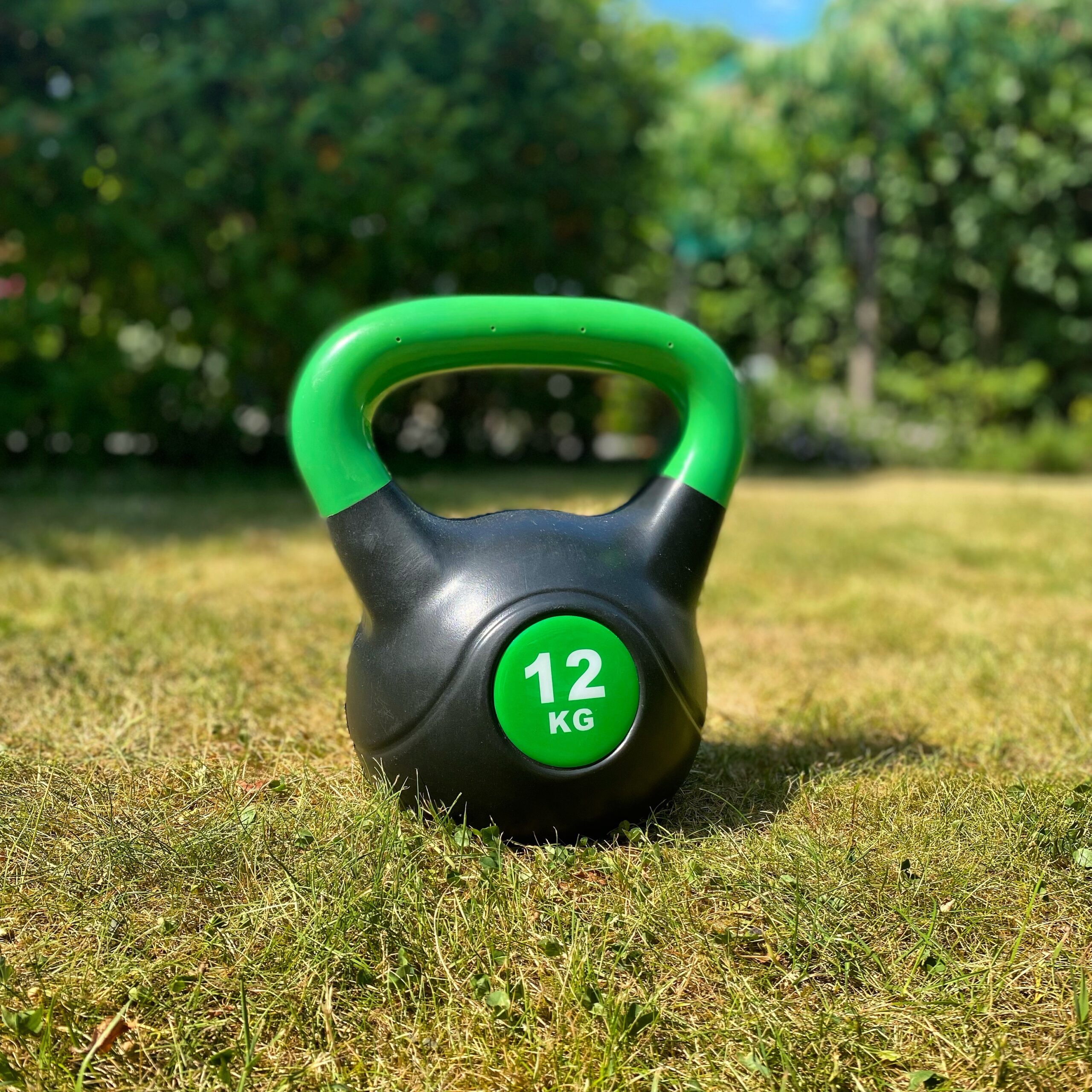 Black kettlebell with a green handle, weighing 12 kg, placed on grass.