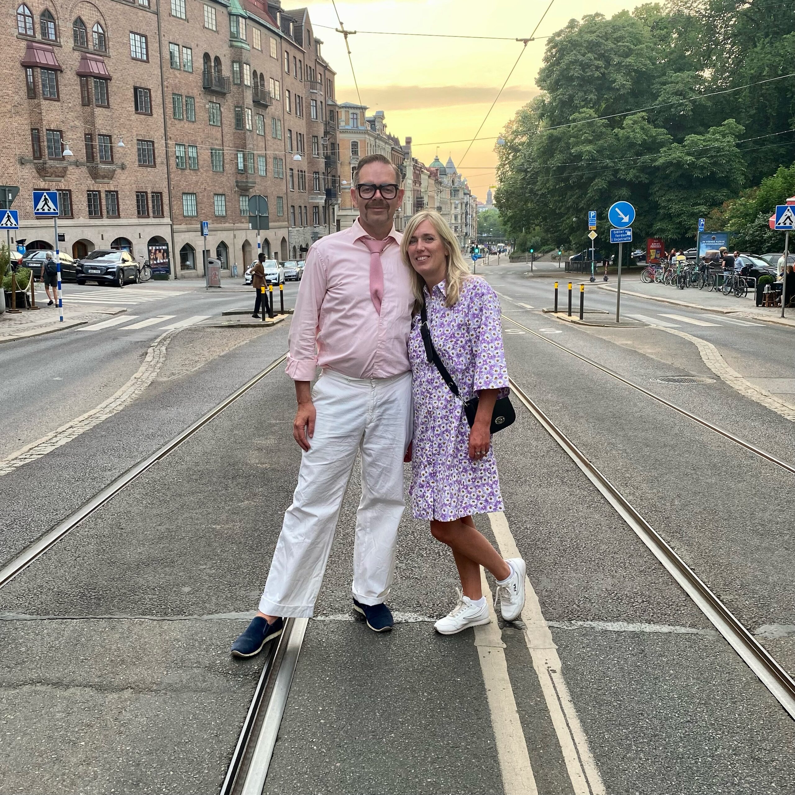 A man and a woman standing on tram tracks in an urban setting during sunset.