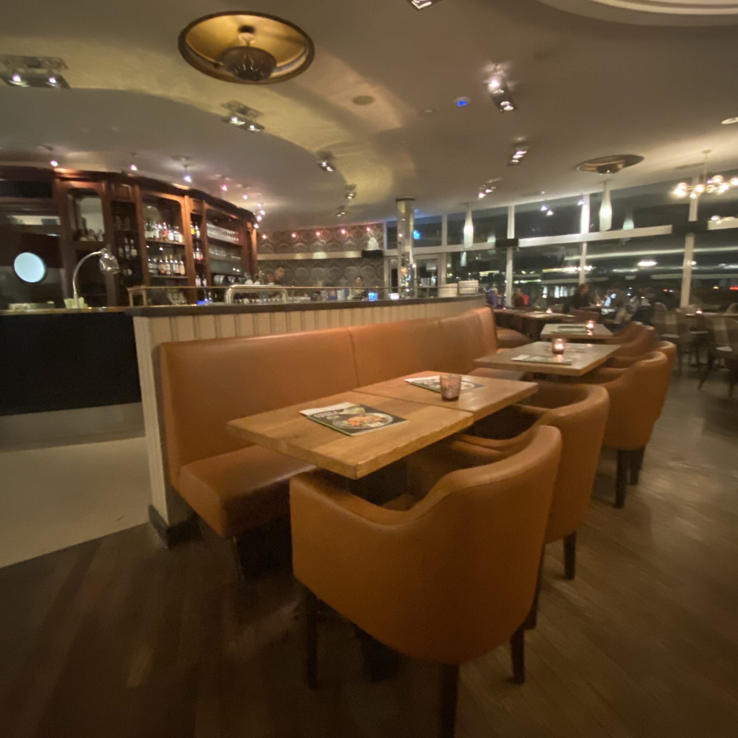Interior view of a restaurant featuring brown leather seating and wooden tables in a modern setting.