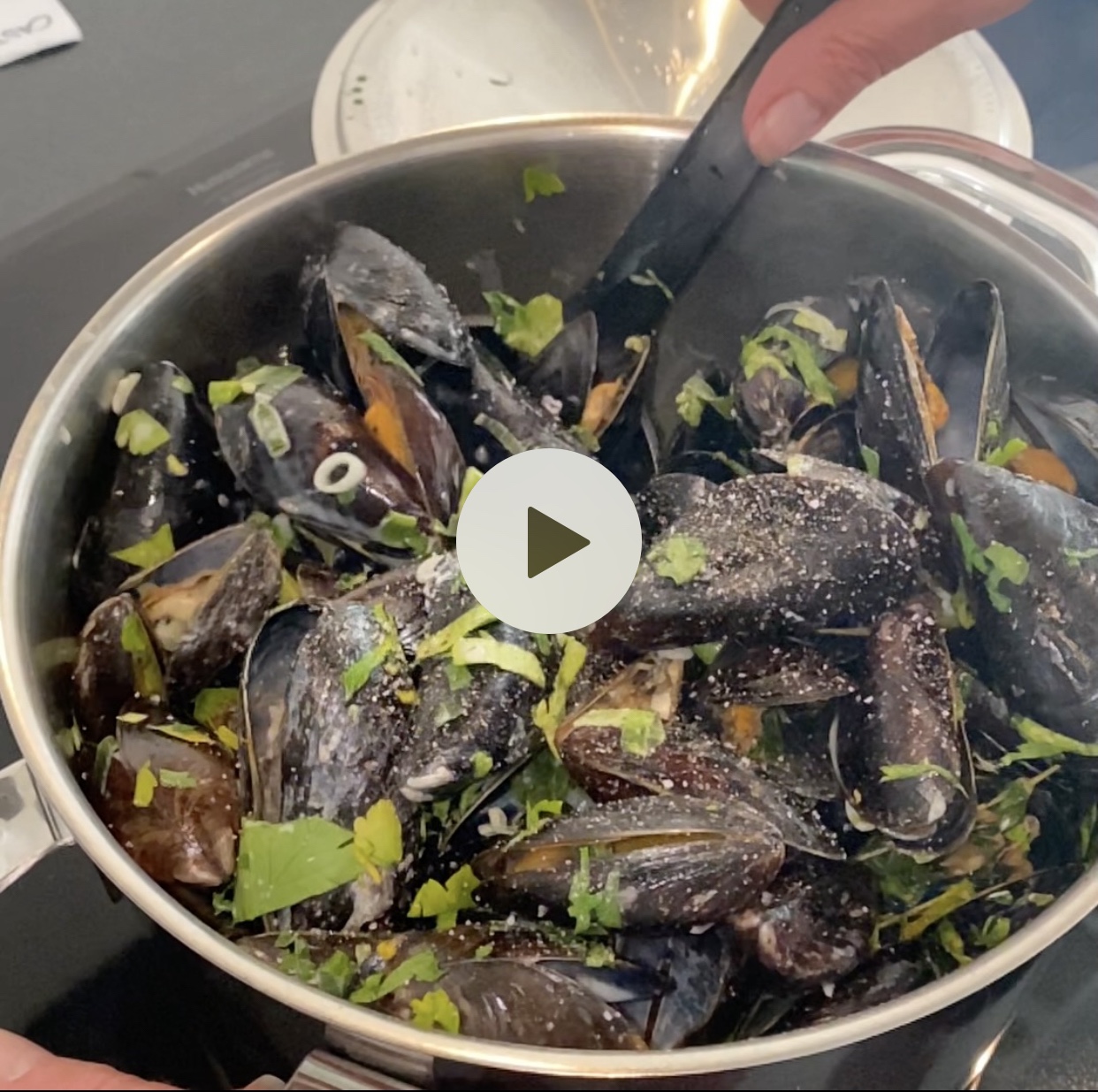 A pot filled with cooked mussels garnished with herbs and spices, ready for serving.