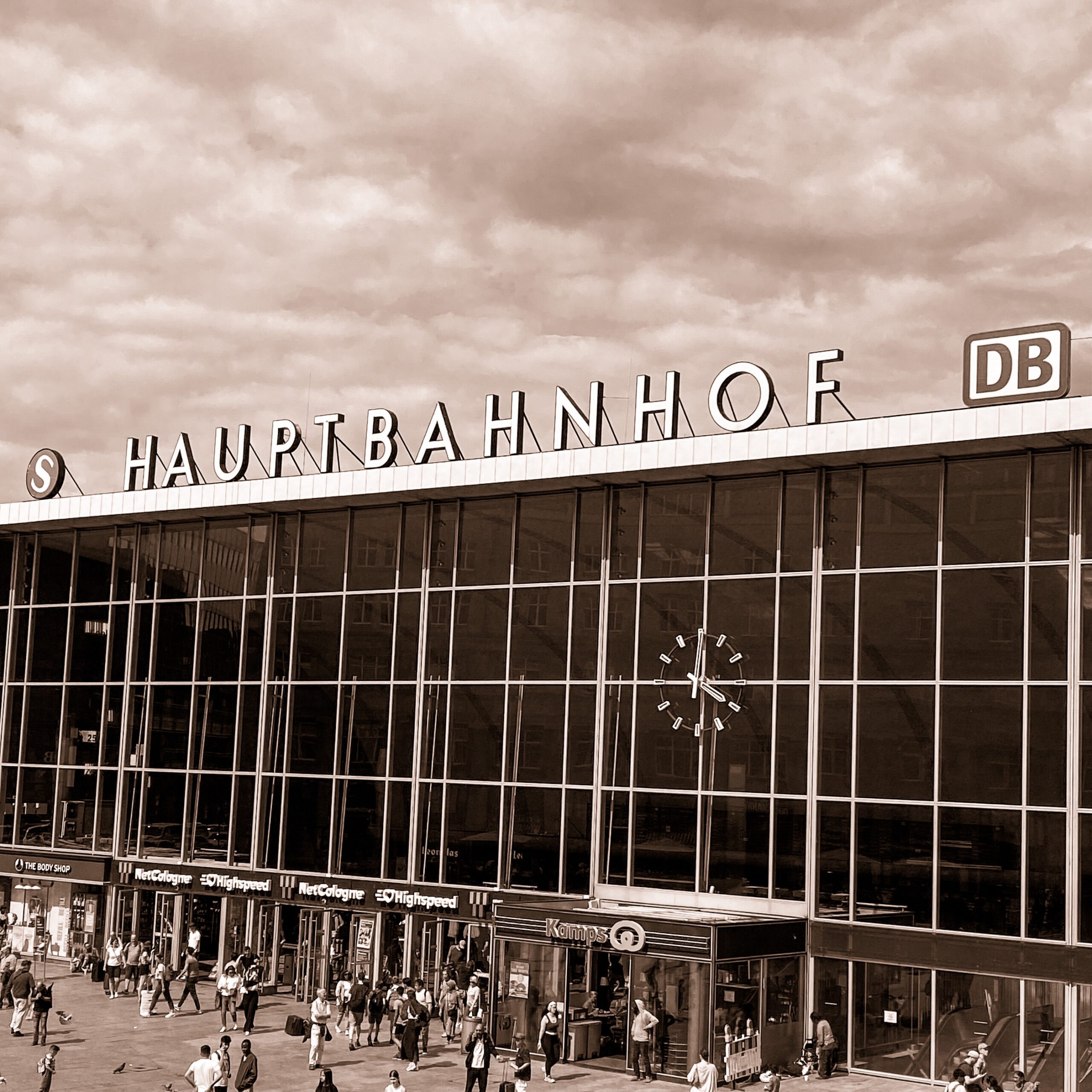 Main entrance of Hauptbahnhof railway station with large clock and people walking outside.
