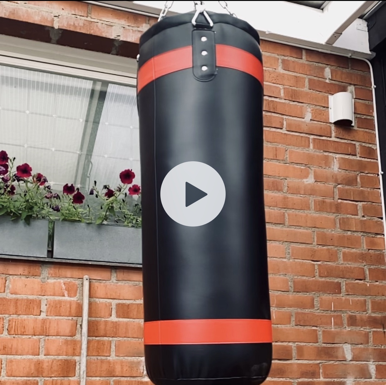 Black and red heavy punch bag suspended from a ceiling, suitable for boxing training.