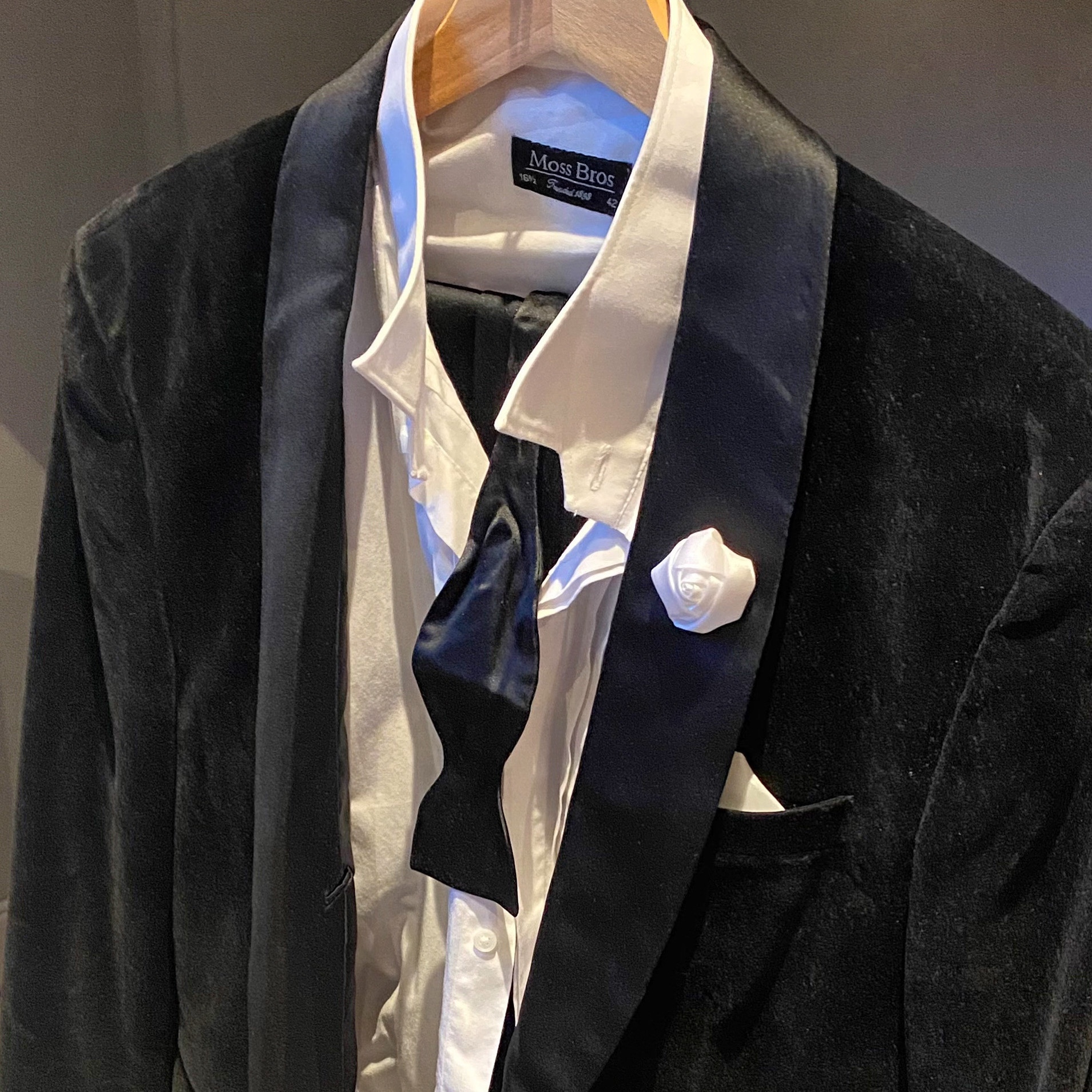 Black velvet tuxedo jacket with a white shirt and black bow tie, featuring a white rose boutonnière.
