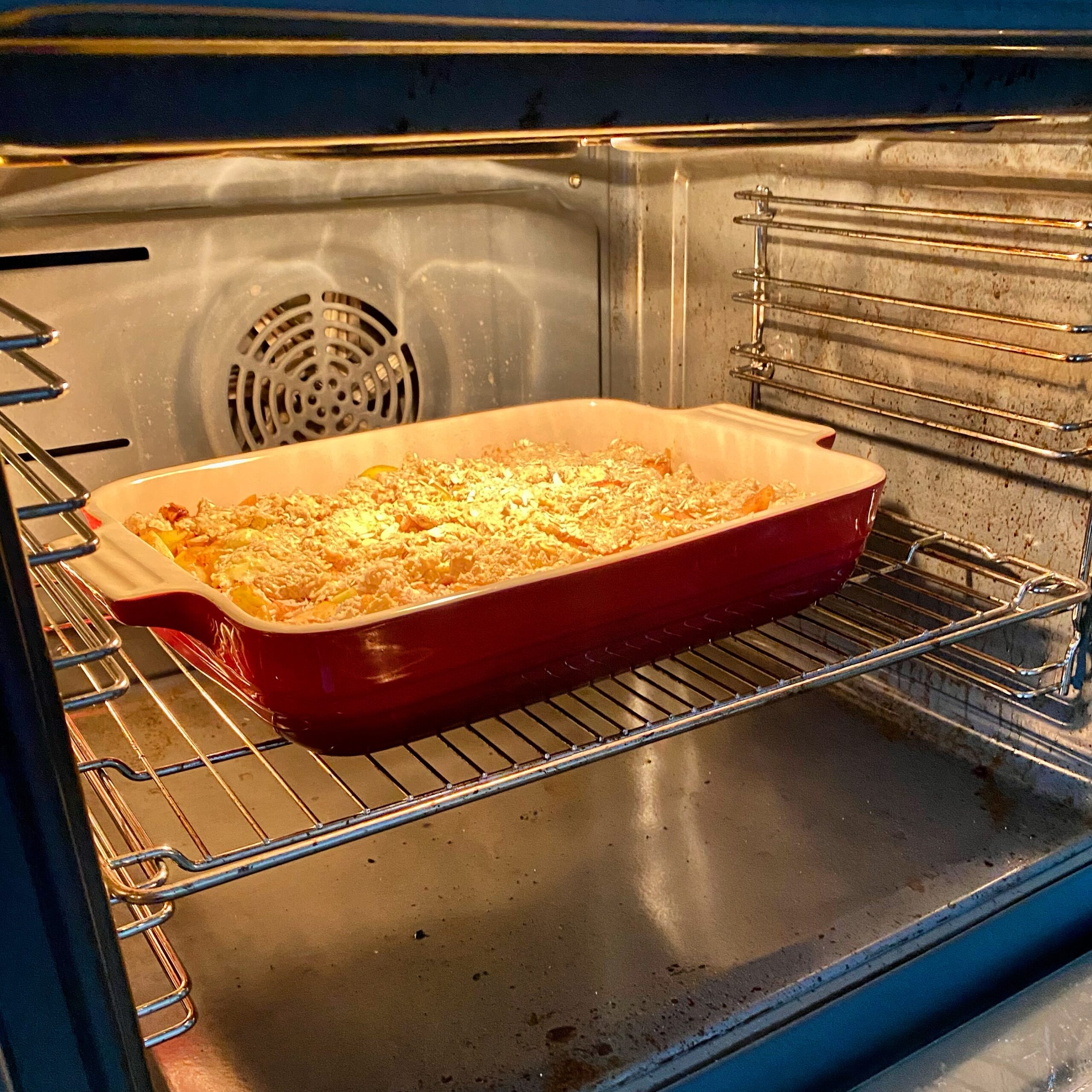 Freshly baked apple pie in a red ceramic dish placed inside an oven with visible heat and light.