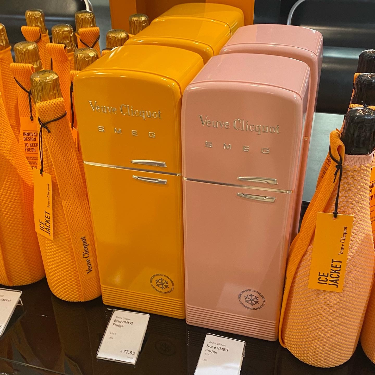 Orange and pink SMEG refrigerators branded with Veuve Clicquot, displayed alongside champagne bottle jackets.