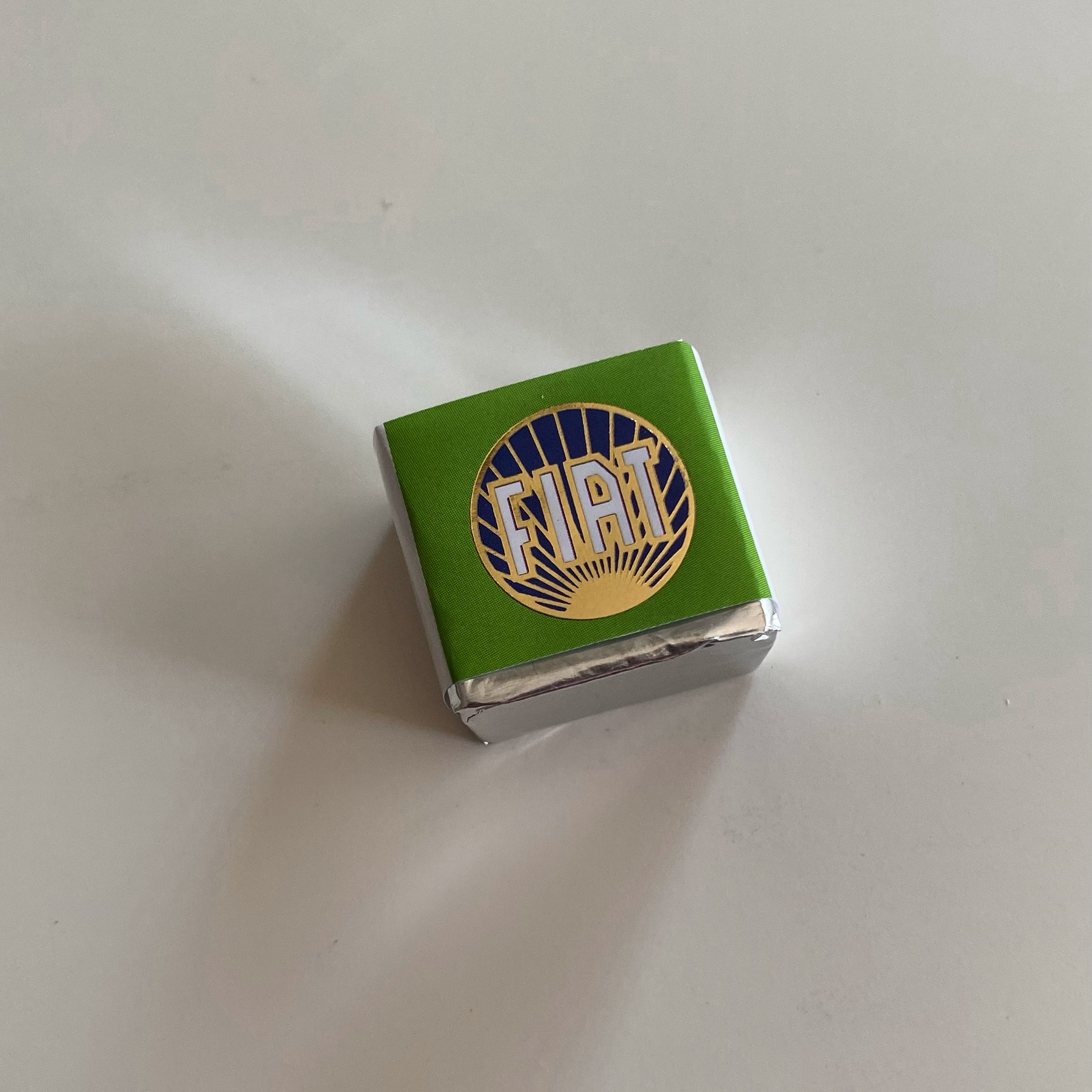 Small green box with a blue and gold Fiat logo on the top, resting on a light surface.