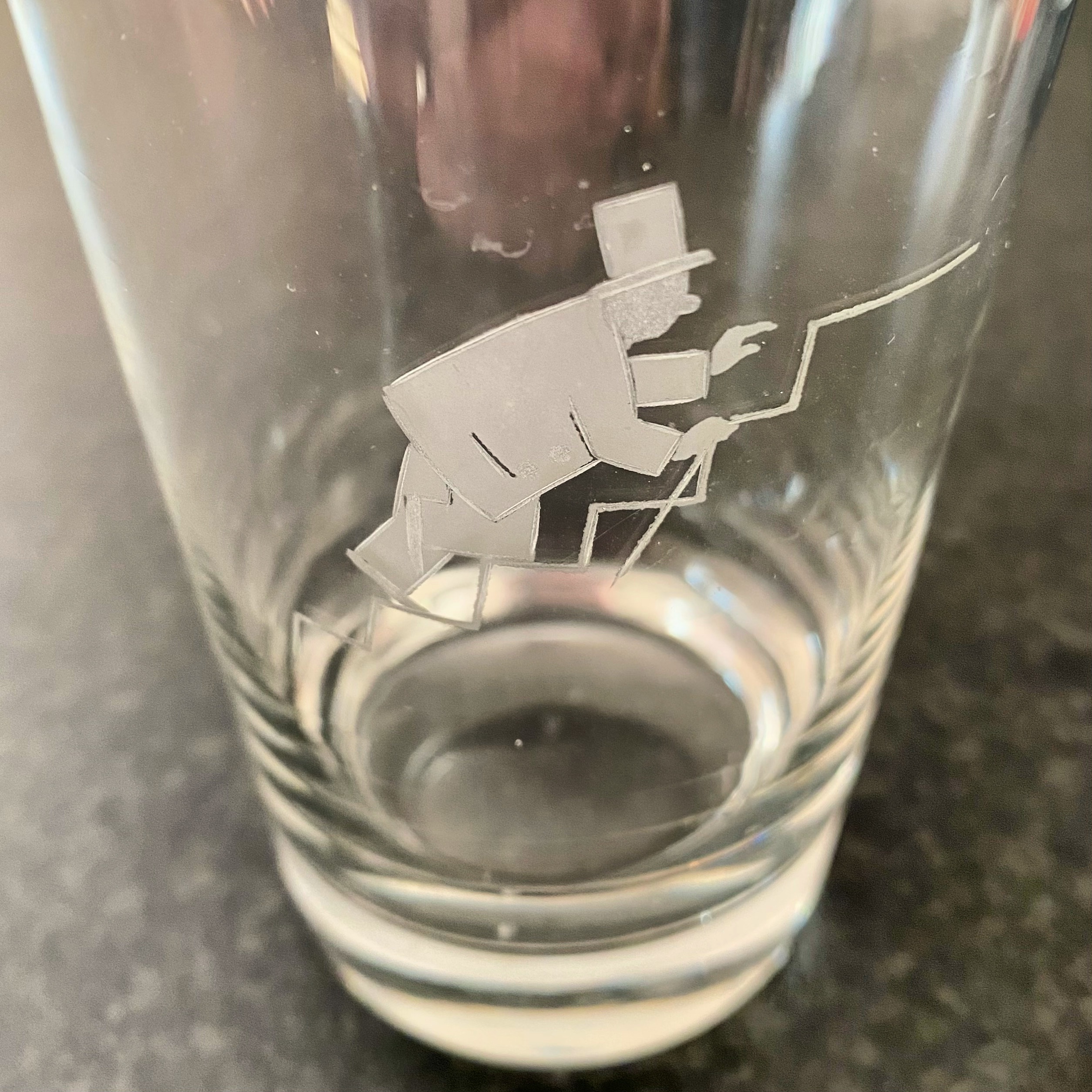Clear glass tumbler with an etched illustration of a man in a top hat climbing a zigzag line.