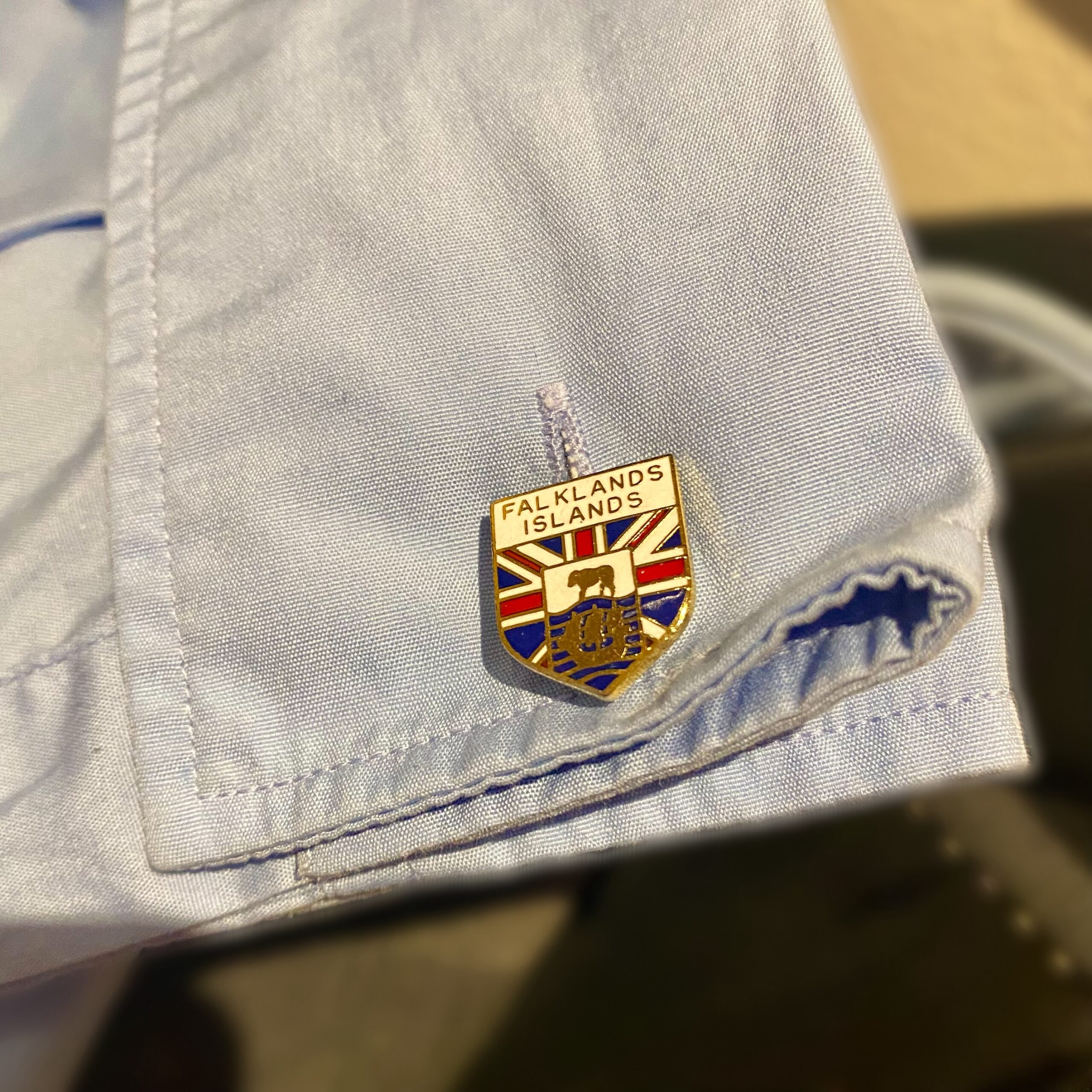 Falkland Islands badge pinned on a light blue shirt cuff, featuring the Union Jack and coat of arms.