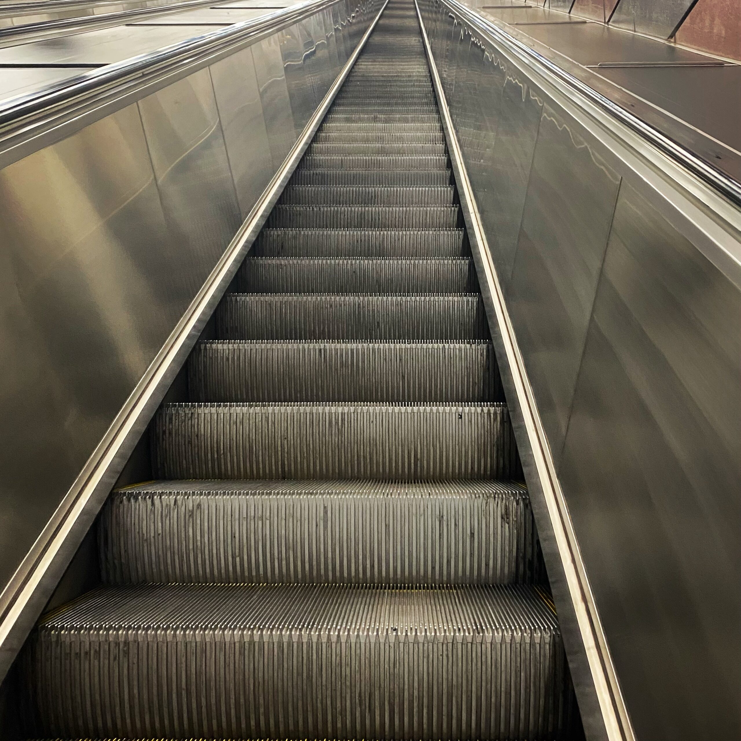Escalator steps leading downwards in a metallic and modern design, showcasing a clean and polished surface.