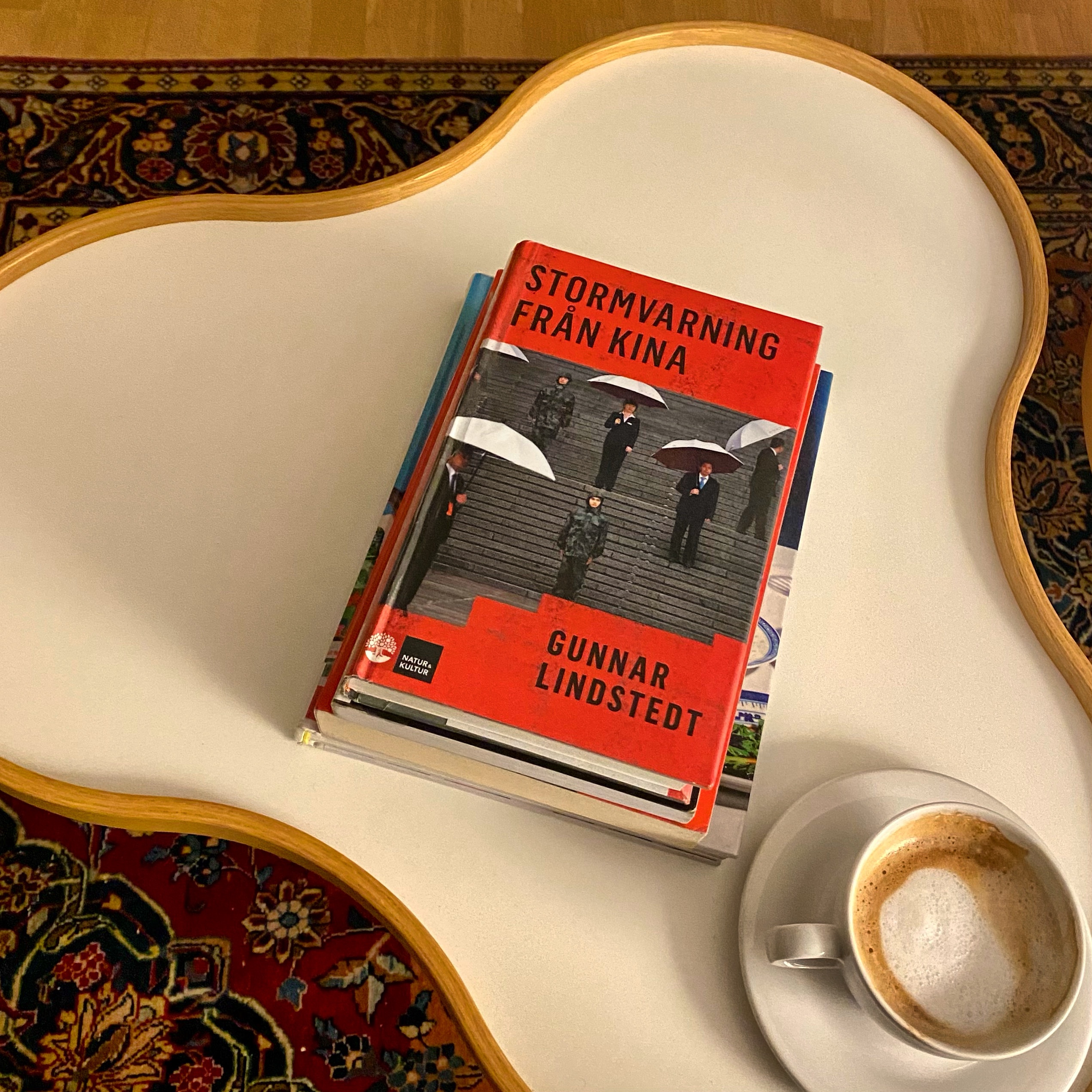 Book titled 'Stormvarning Från Kina' by Gunnar Lindstedt placed on a coffee table beside a cup of espresso.