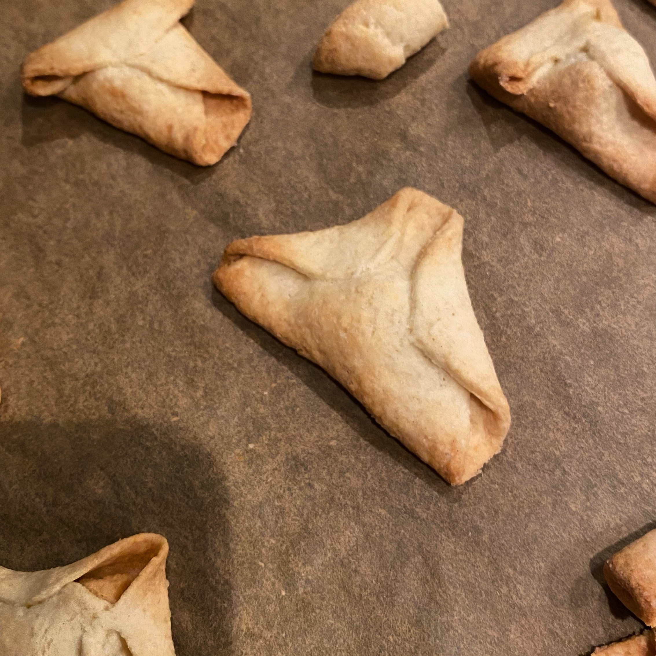 Baked pastry pieces arranged on a baking tray with a golden-brown colour and triangular shape.