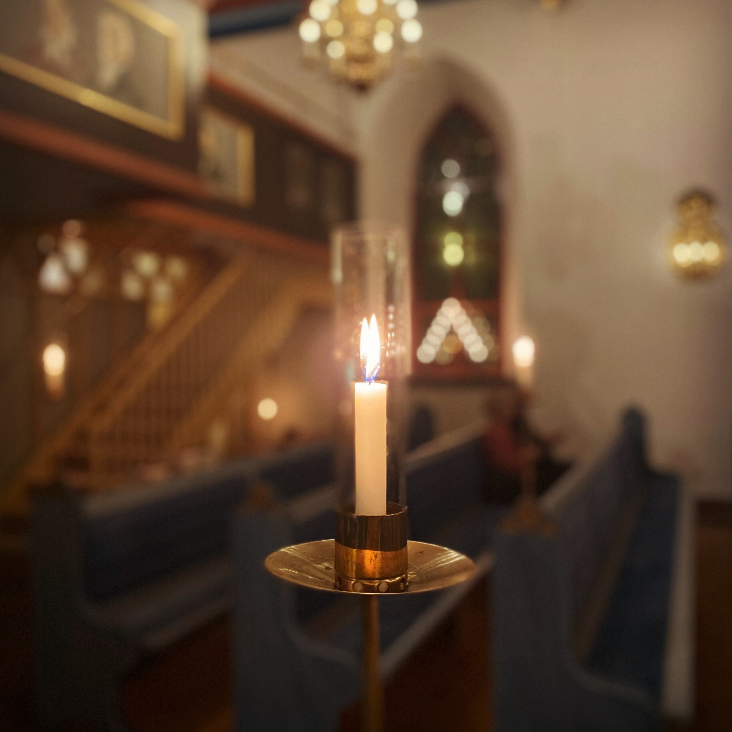 Candle in a glass holder illuminating a dimly lit interior with pews and decorative elements.
