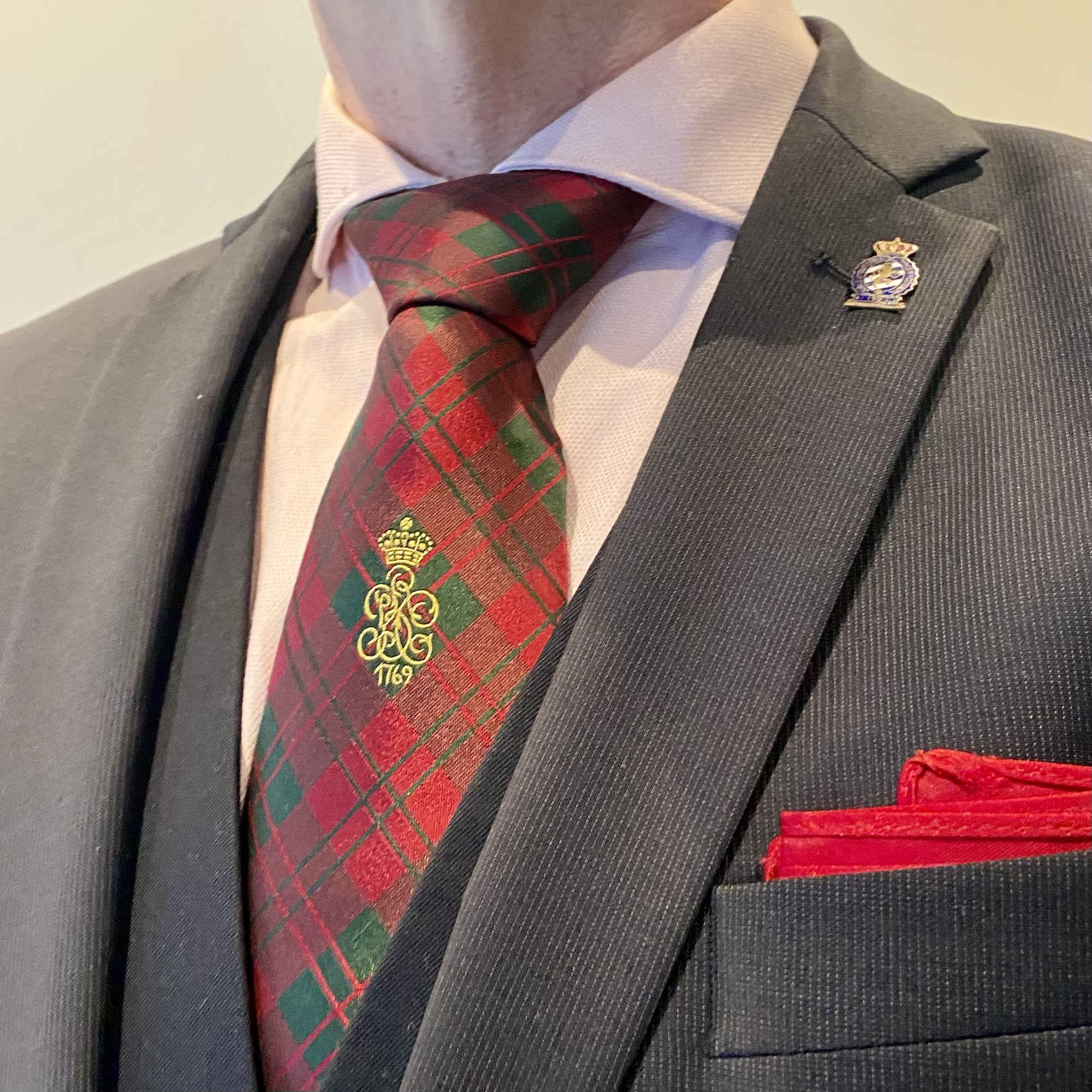 Man wearing a tartan tie with a green and red pattern, complemented by a lapel pin and pocket square.