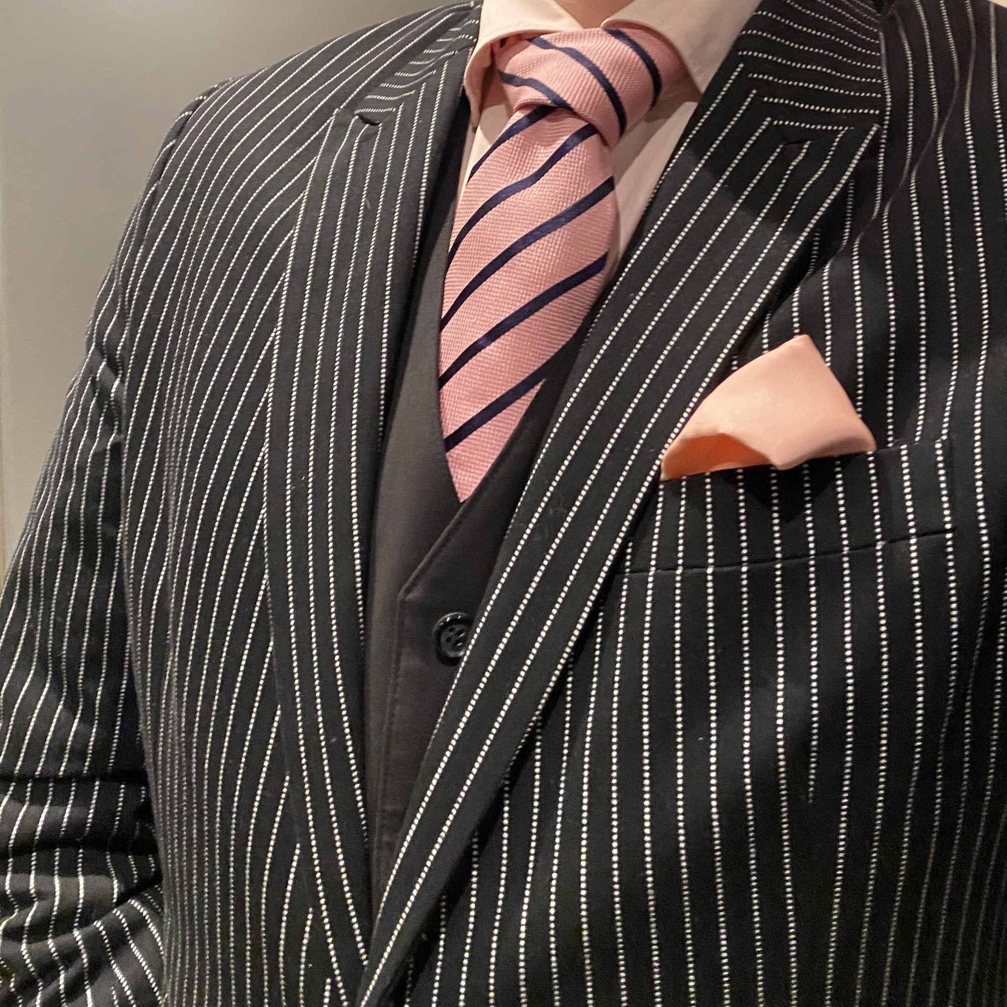 Man dressed in a pinstripe suit with a pink striped tie and a pocket square.