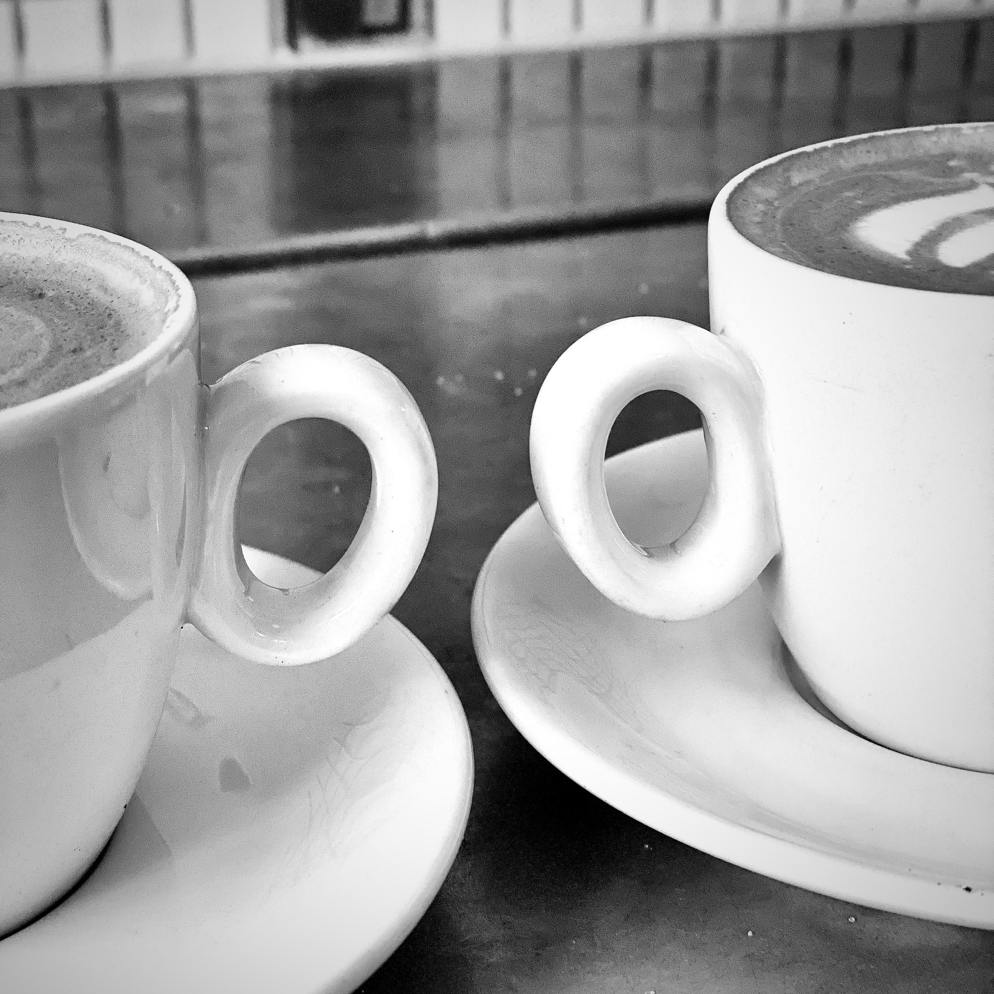 Two white coffee cups with distinctive loop handles on saucers, one with latte art on top.