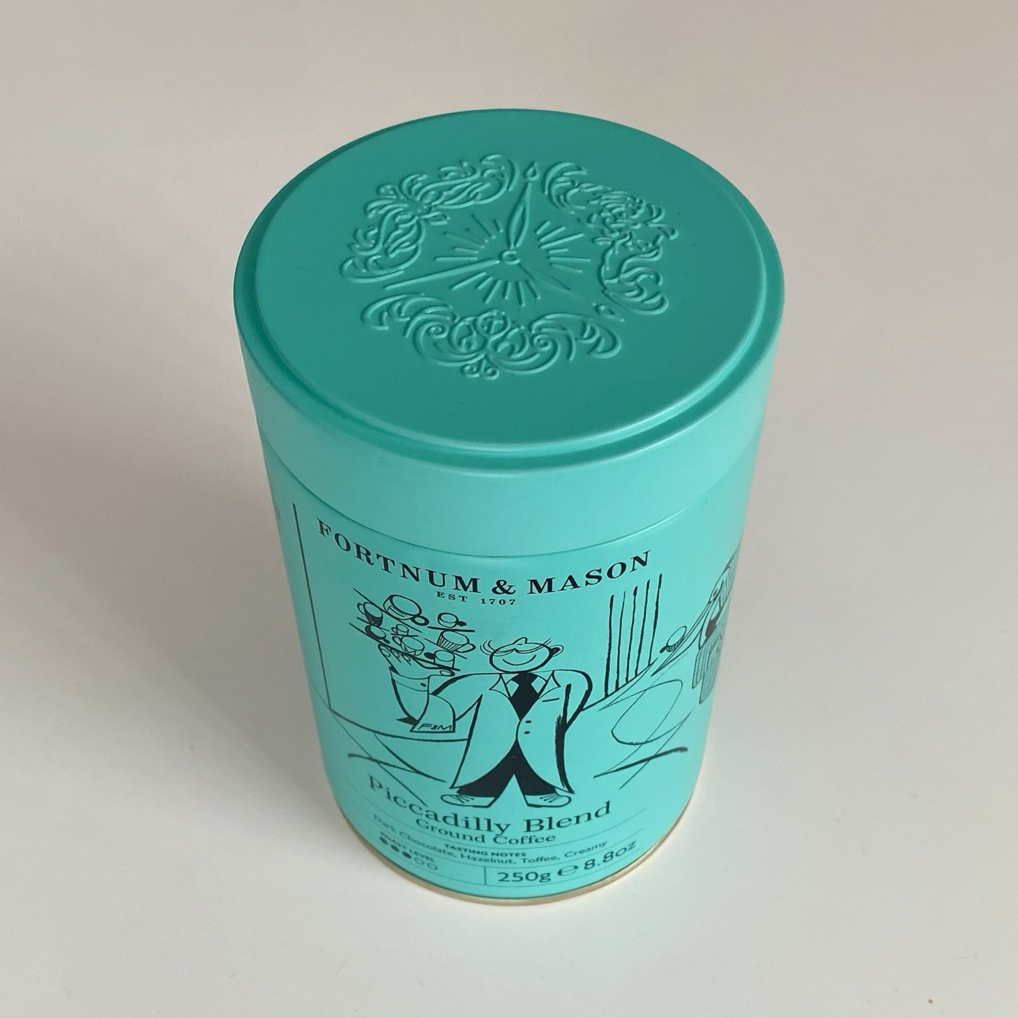 Turquoise cylindrical tin of Fortnum & Mason Piccadilly Blend ground coffee with decorative lid design.
