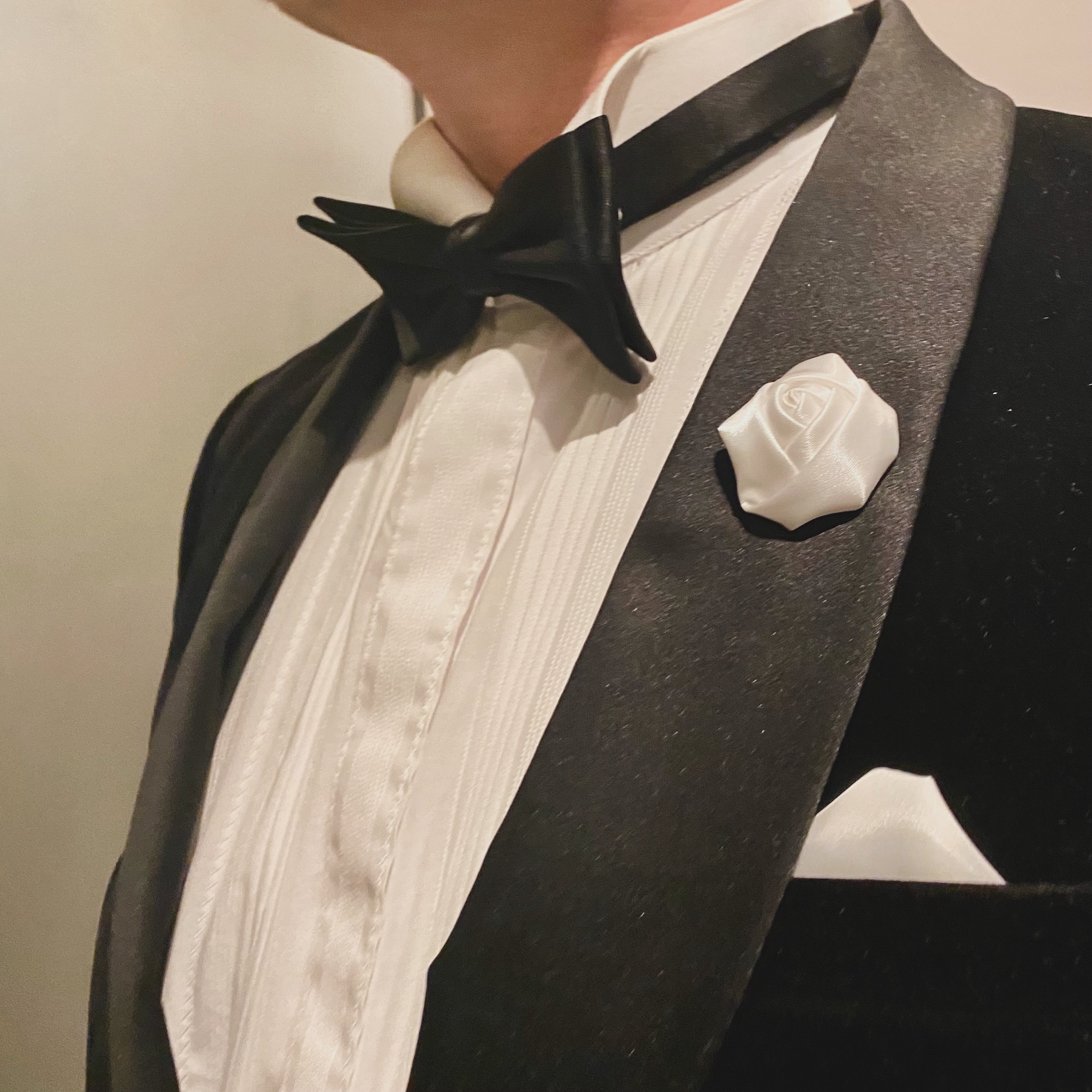 Close-up of a man in a black tuxedo with a white rose lapel pin and bow tie.