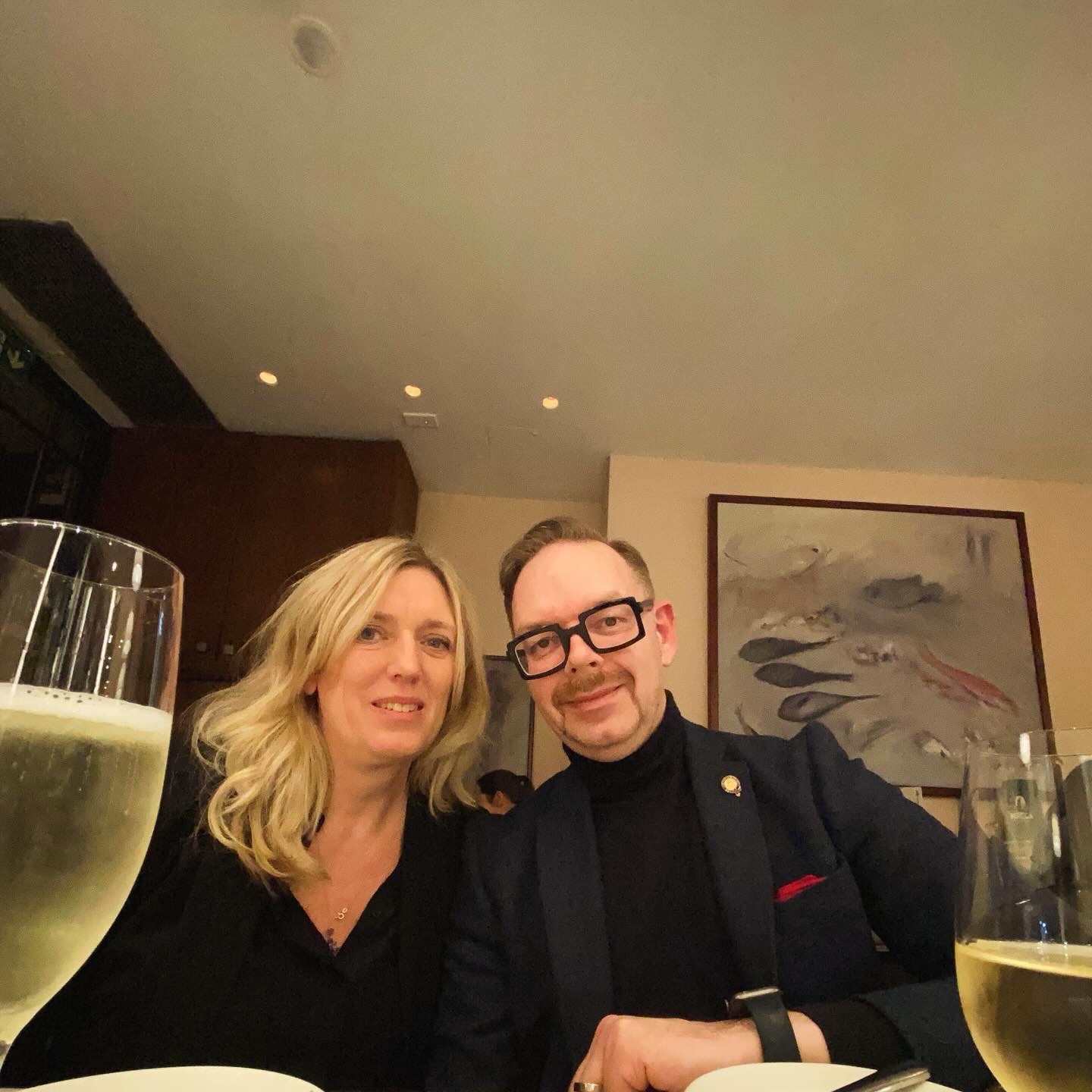 A man and a woman posing together at a dining table with glasses of champagne in front of them.