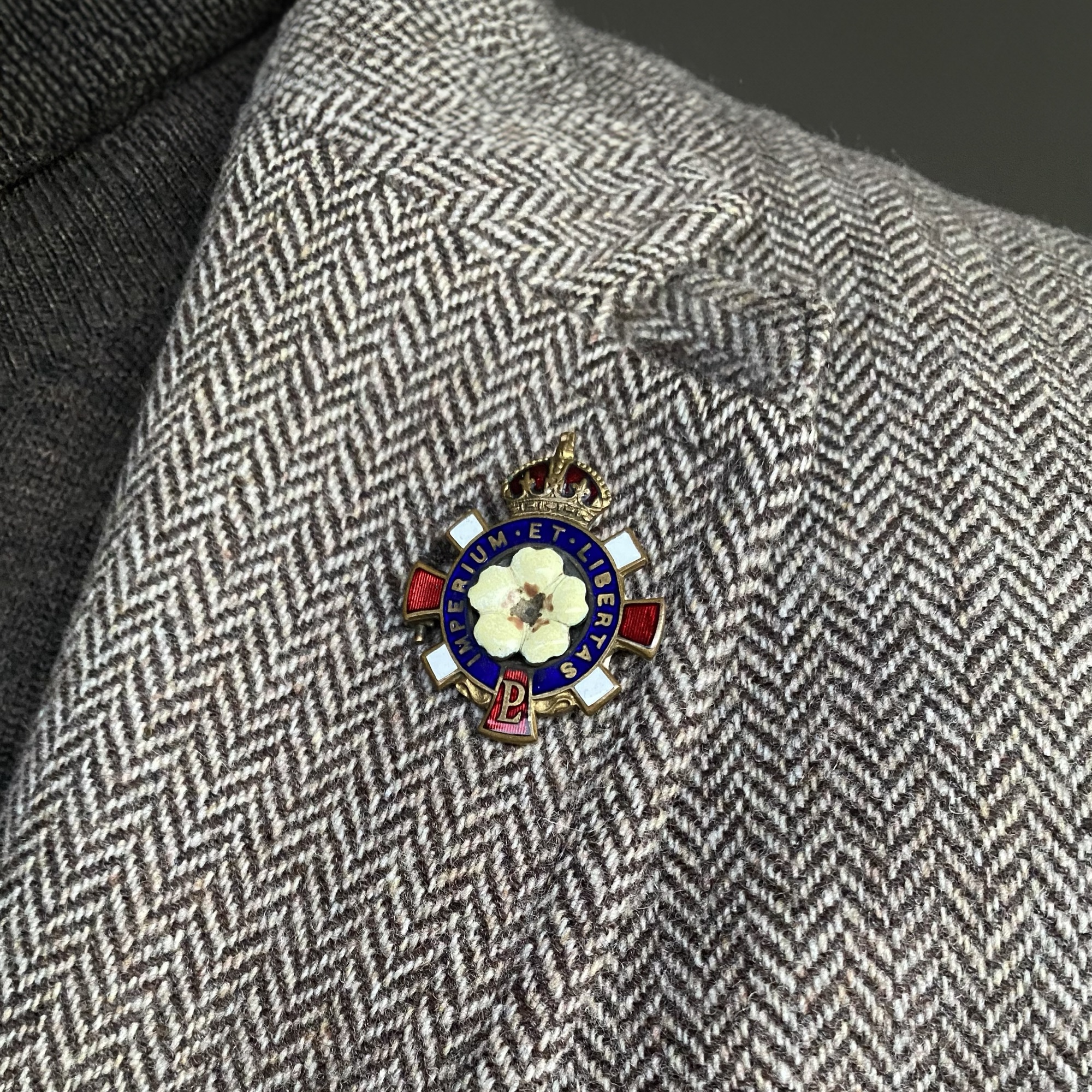 A vintage brooch from the 1920s featuring a white rose and blue and red enamel detailing.