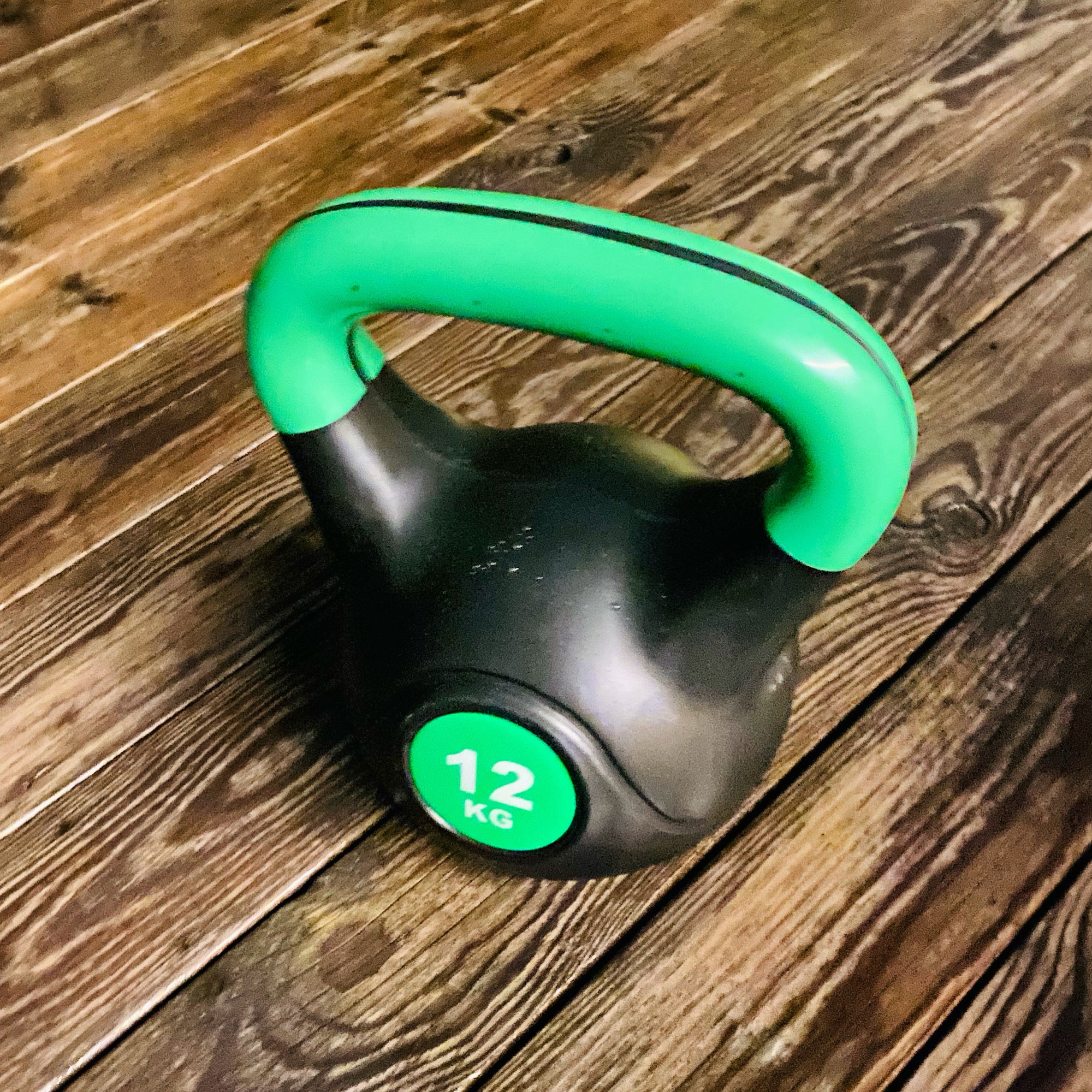 Black kettlebell with a green handle and a weight of 12 kg on a wooden floor.