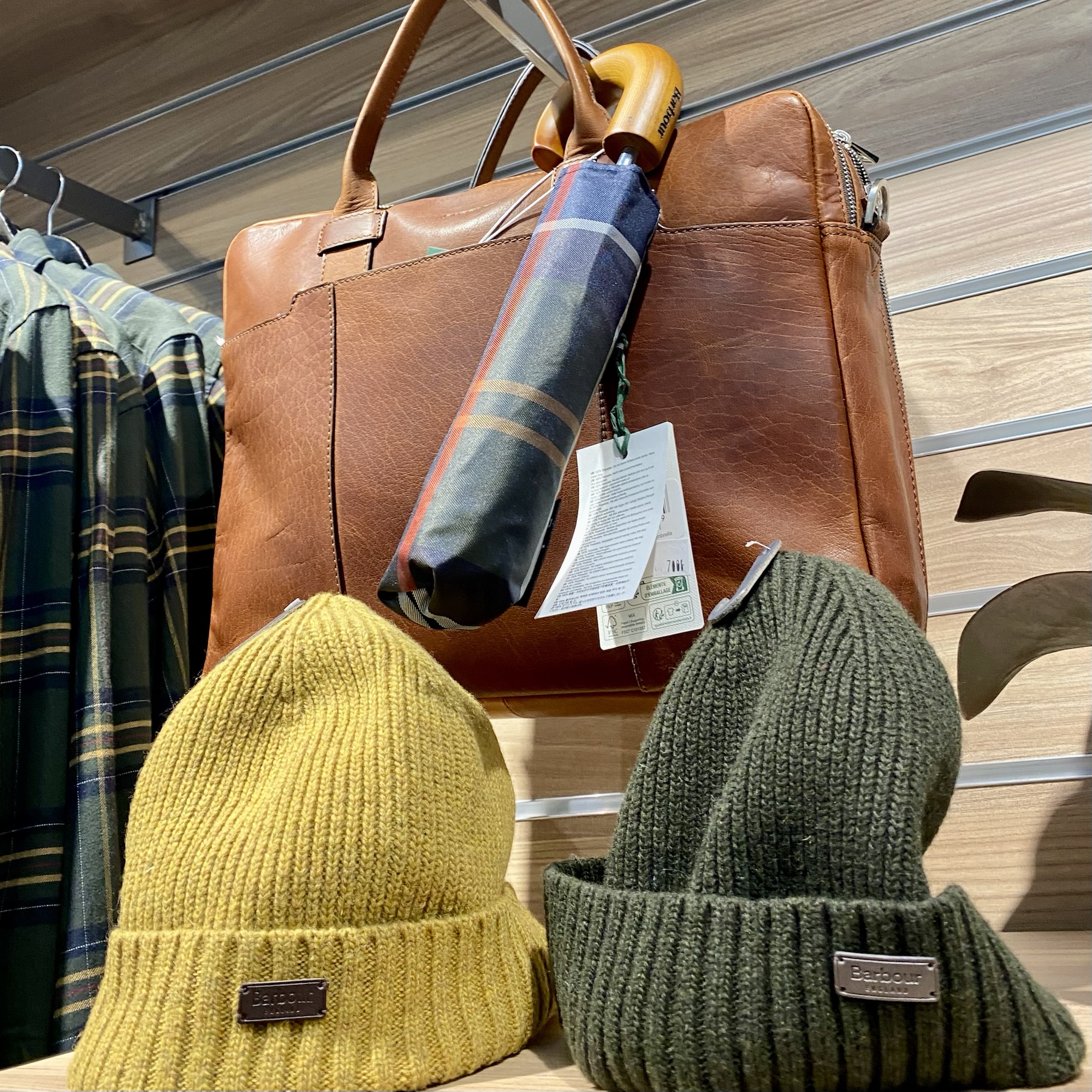 Brown leather handbag with an umbrella and two knitted beanie hats in yellow and green displayed on a shelf.