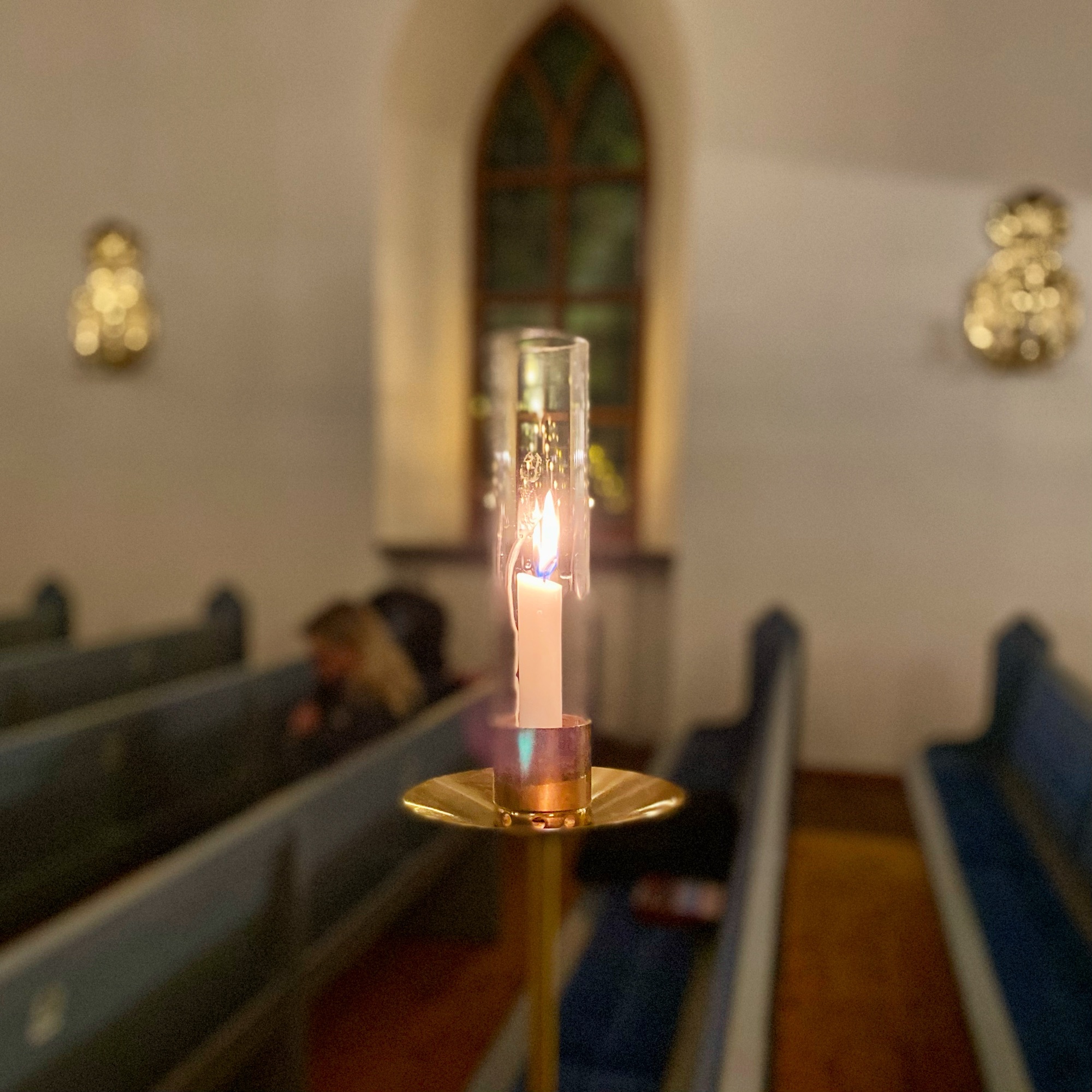 Candle on a brass holder with a lit flame in a church interior during a morning service.
