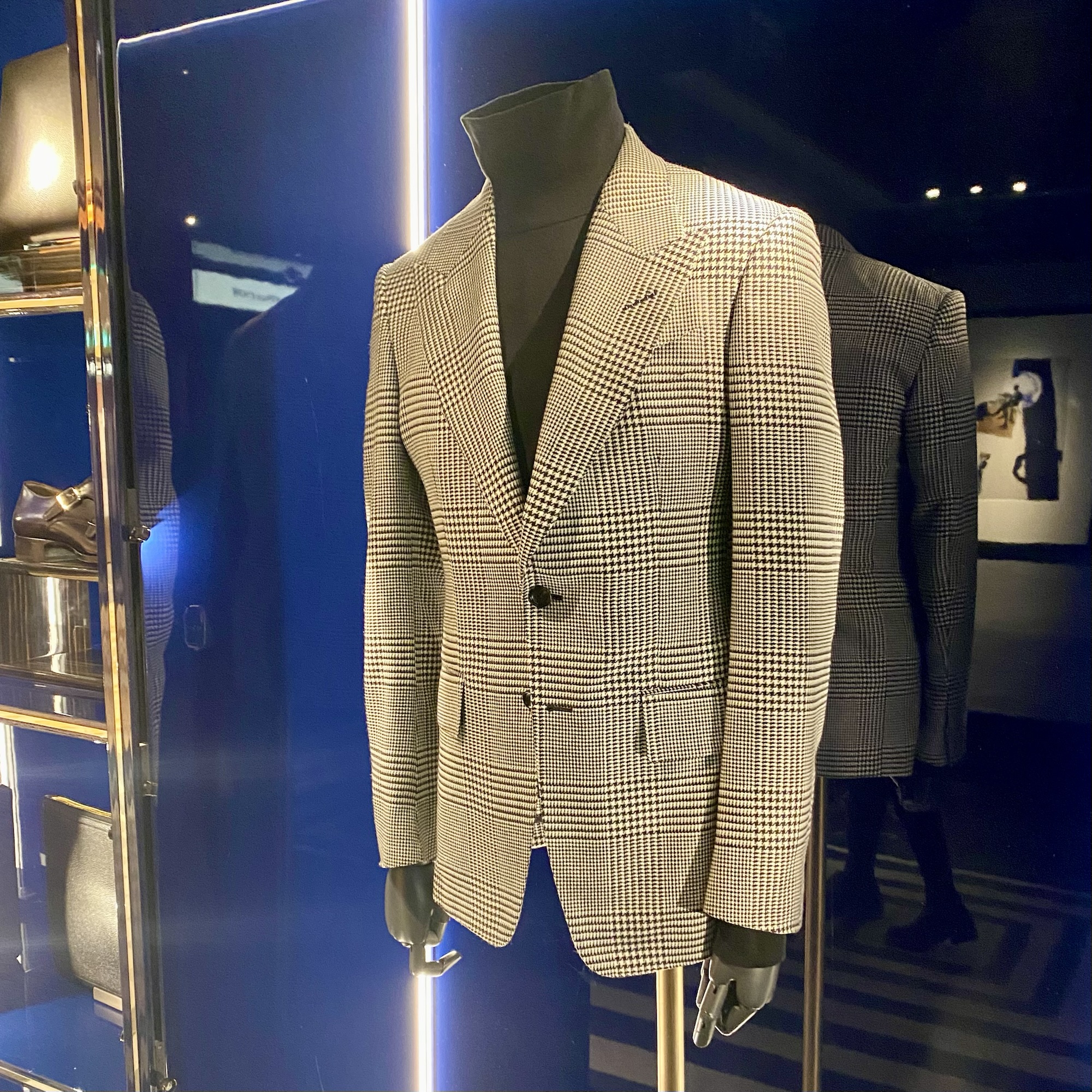 Tailored check-patterned blazer displayed on a mannequin against a dark background.