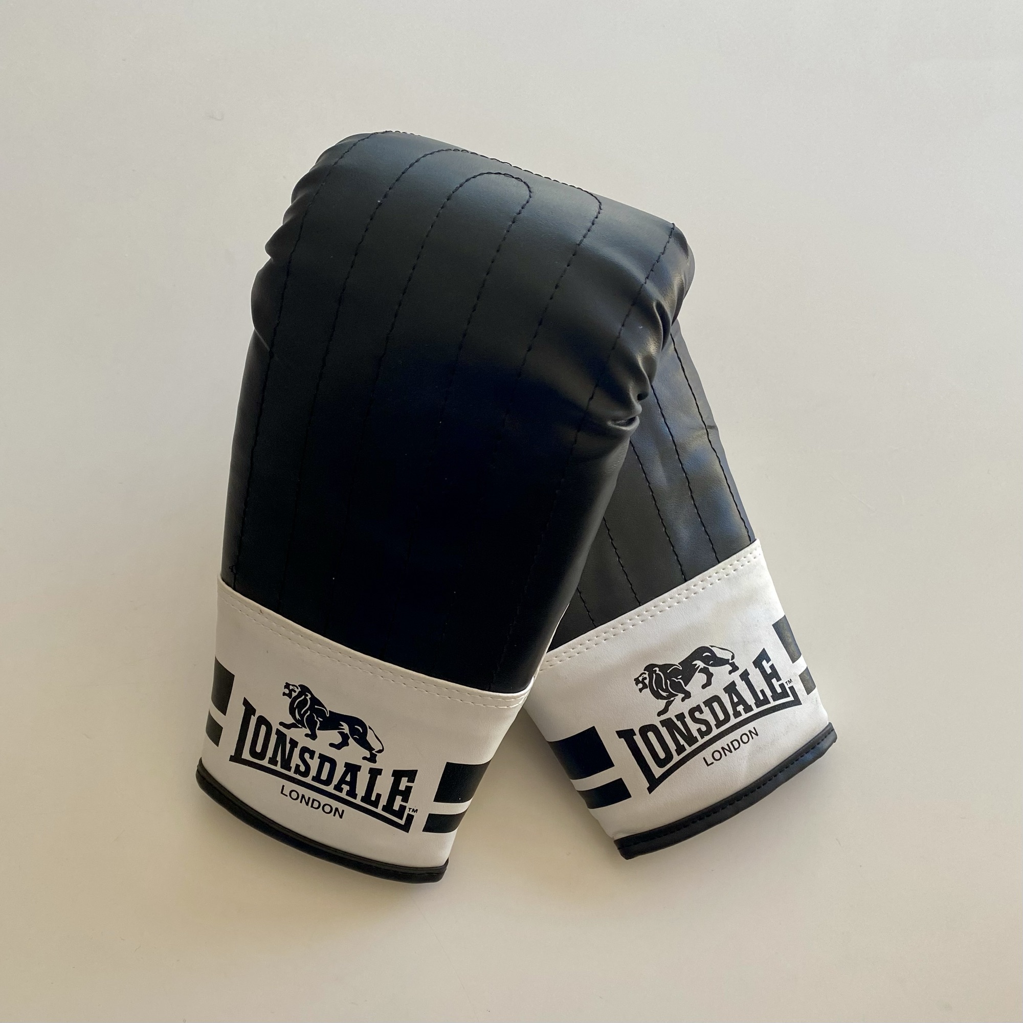 Black and white boxing gloves with Lonsdale branding, positioned on a plain background.