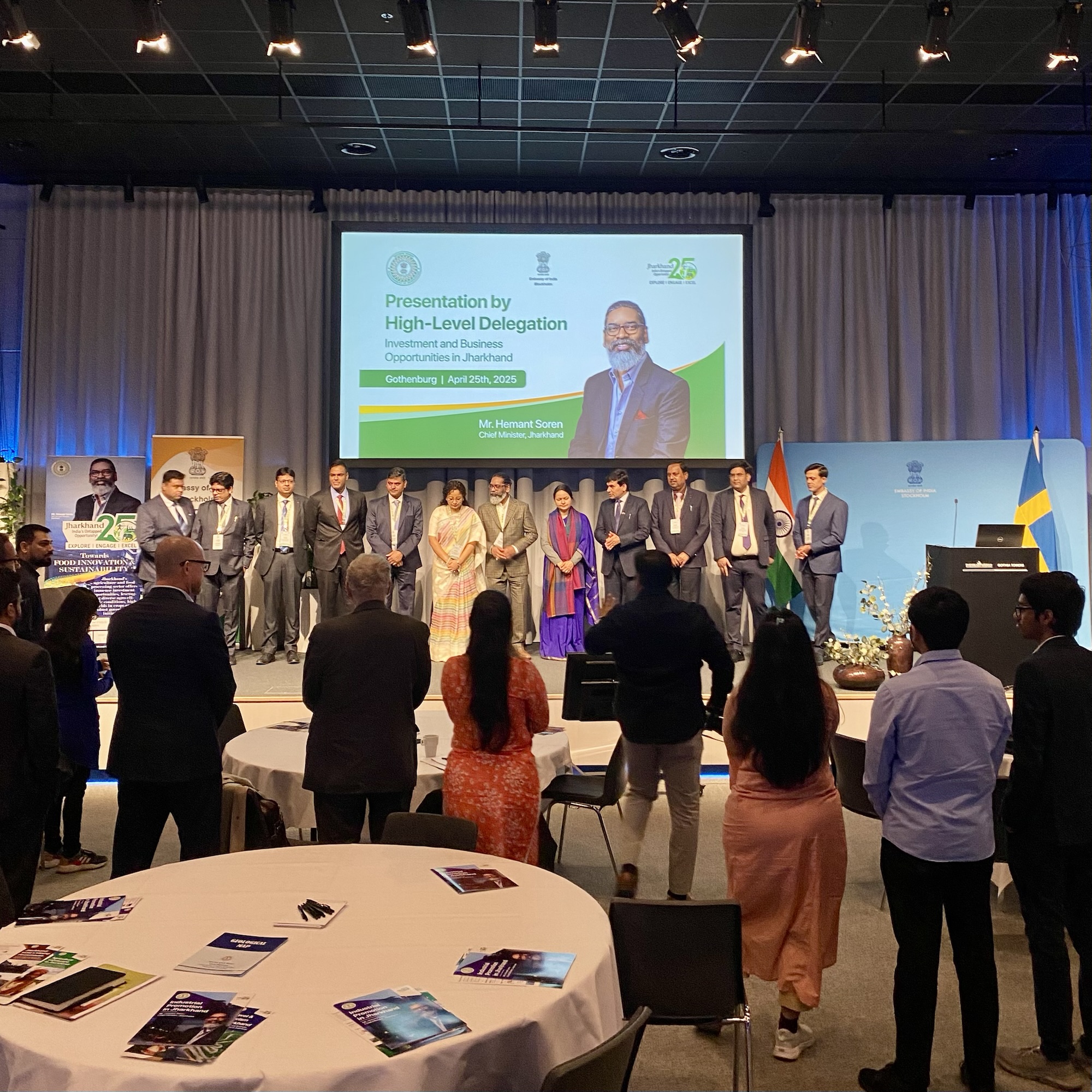 Group of individuals standing in formal attire during a presentation event with a backdrop displaying the Indian and Swedish flags.