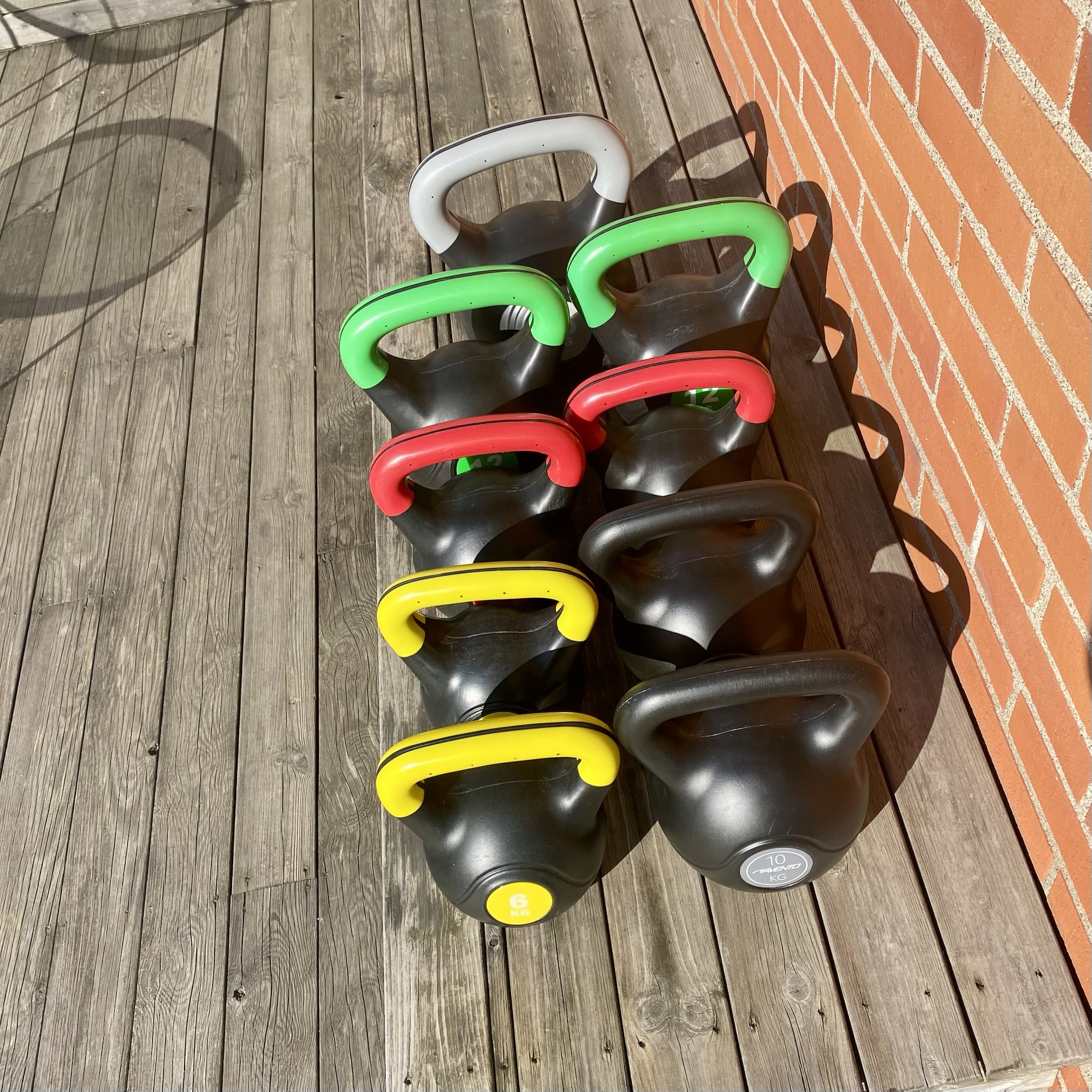 A row of kettlebells in various colours arranged on a wooden surface, showcasing different weights.