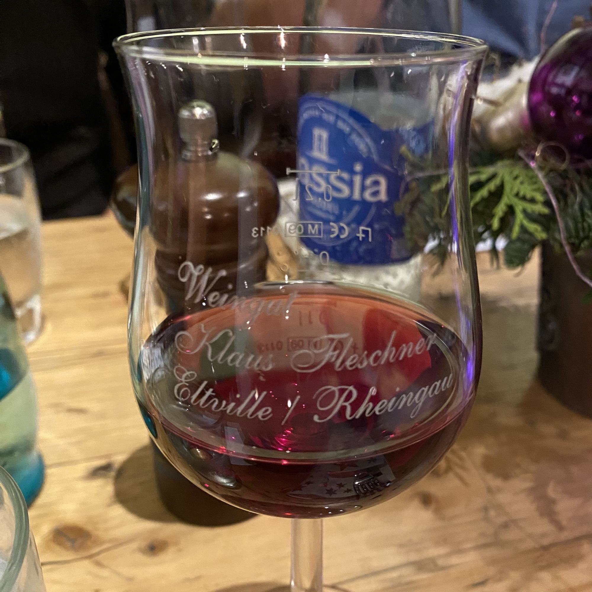 Wine glass with red wine, engraved with 'Weingut Klaus Fleischer, Eltville i. Rheingau' on a wooden table.