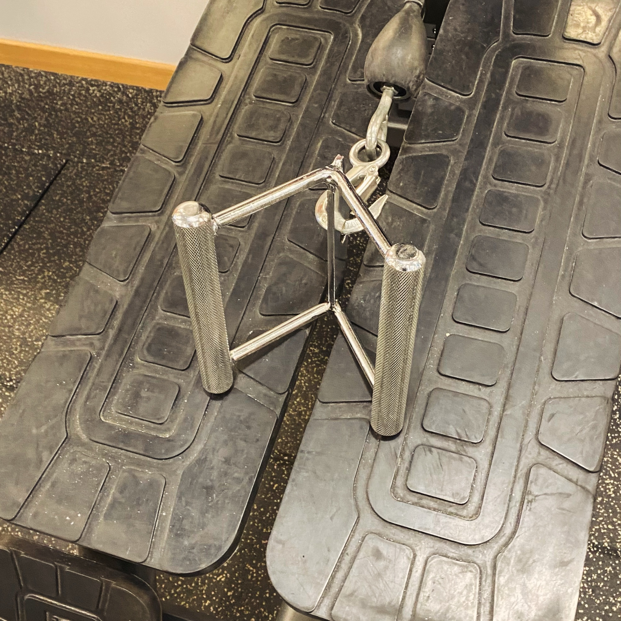 Steel cable attachment with textured grips positioned on a gym bench.