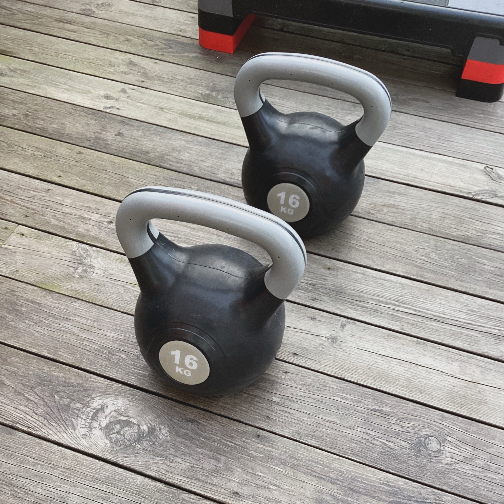 Close view of two black and grey kettlebells marked 16 kg on wooden decking, ready for lifting even on tough days