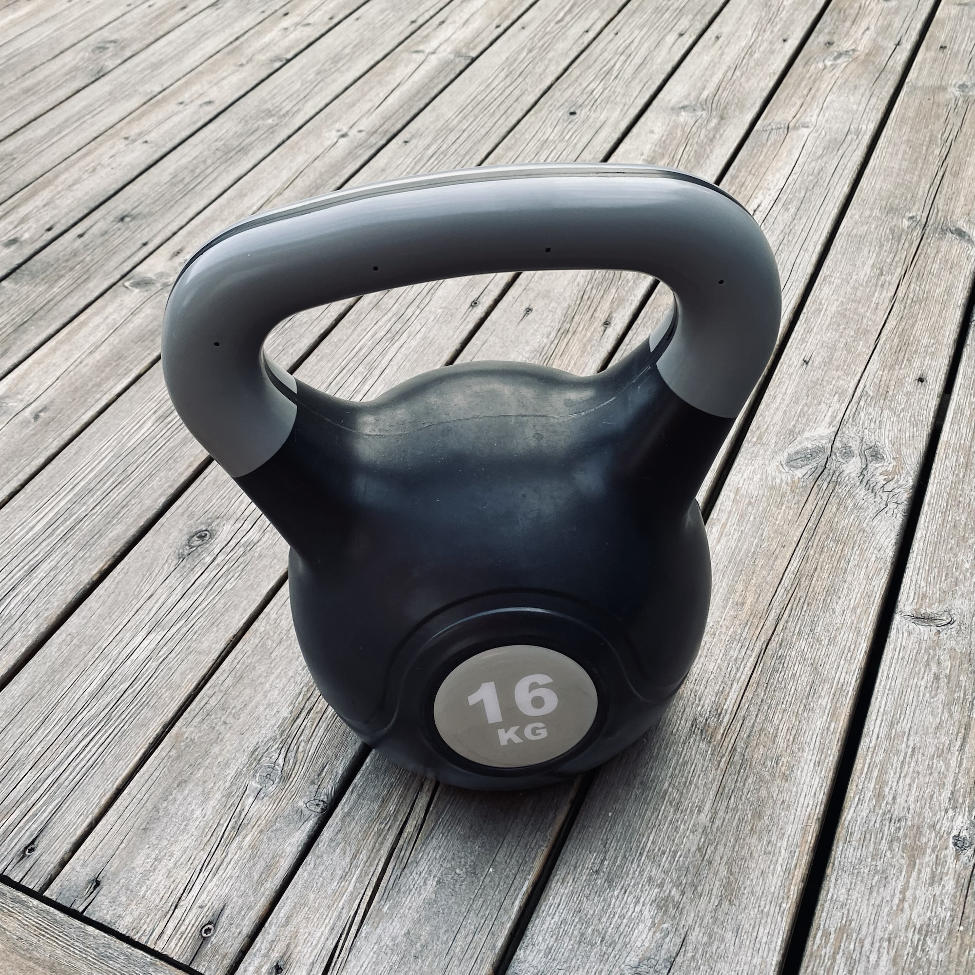 A 16 kg kettlebell rests on a weathered wooden deck, matching the weekend note, “Well, it’s Saturday night,” in a simple fitness snapshot.