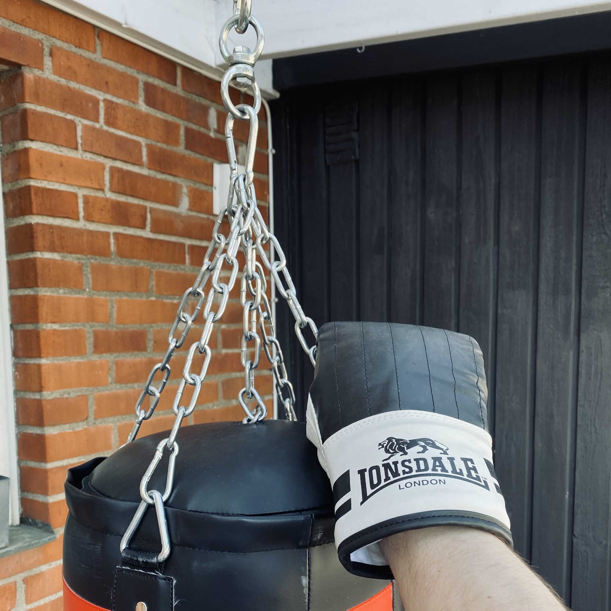 Silver chain hanging beside a brick wall, with a boxing glove marked London in view, linking grit and the warmth of loving arms.