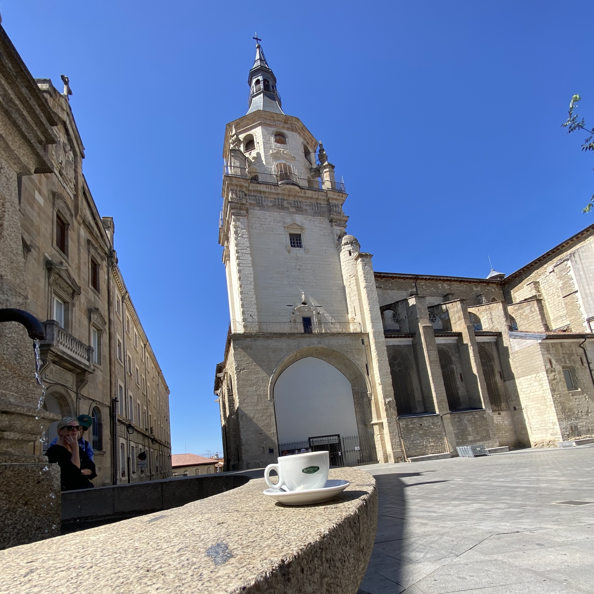 A cortado on a stone ledge sits before the Cathedral of Santa María in Vitoria-Gasteiz under a clear blue sky.
