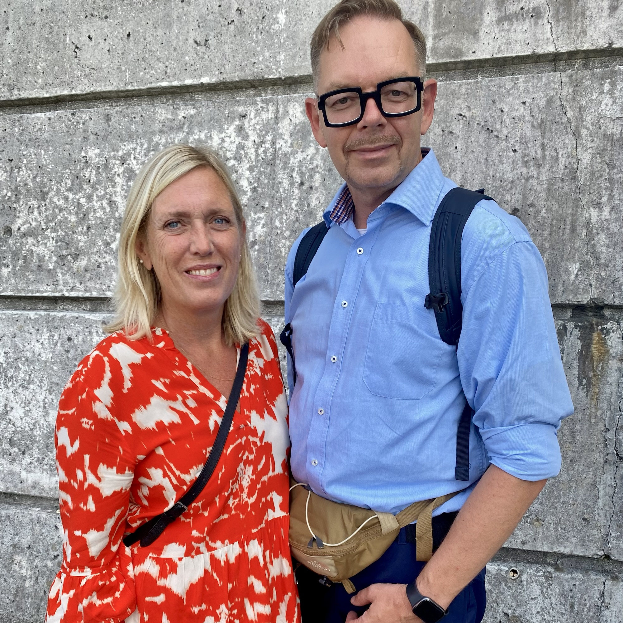 Joakim Dahl stands with a blonde woman by a weathered concrete wall, both dressed for a day out.